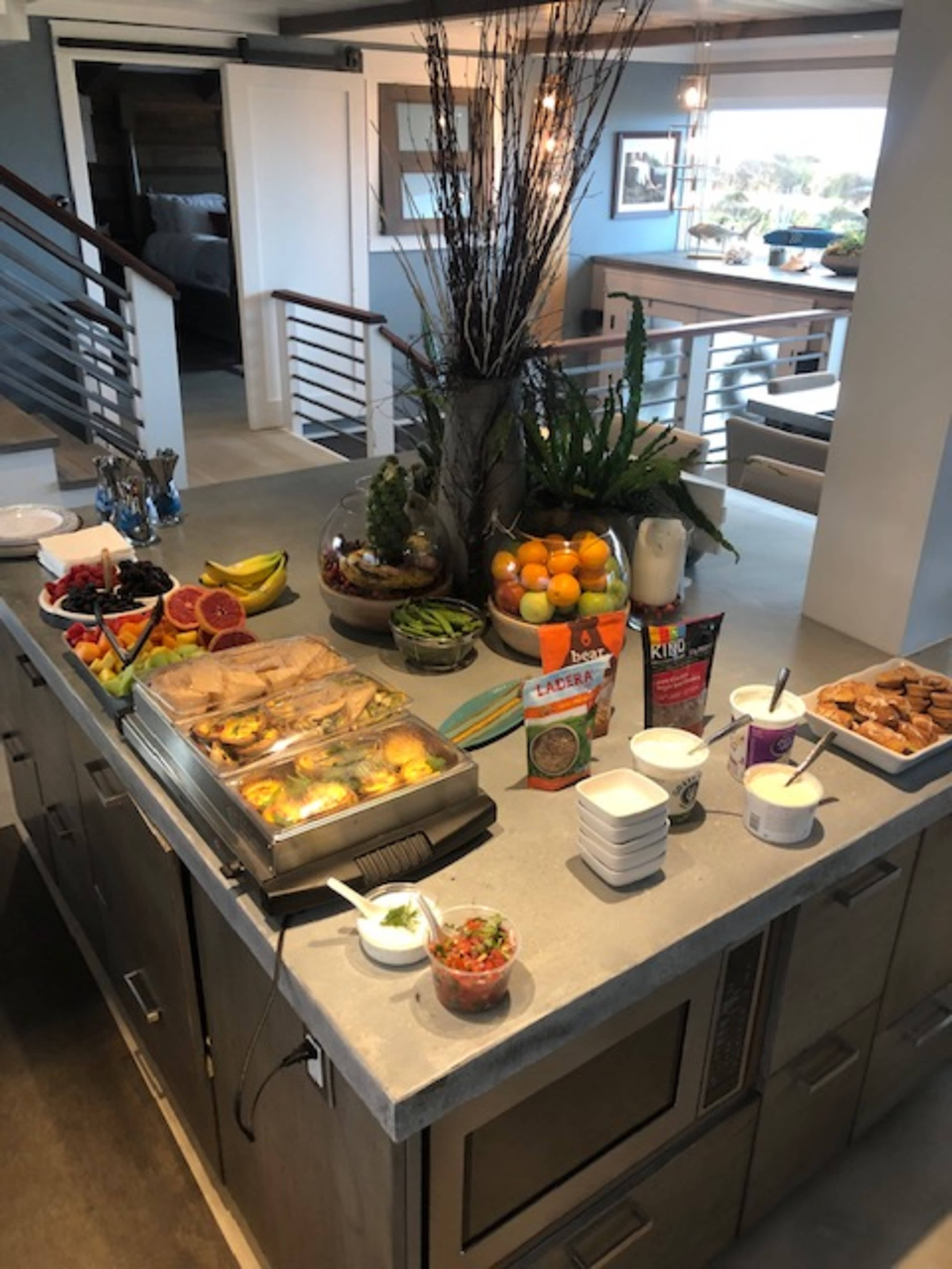 A large kitchen island is laden with a variety of food items, including pastries, fruits, yogurt, and dips, arranged neatly in bowls and trays.