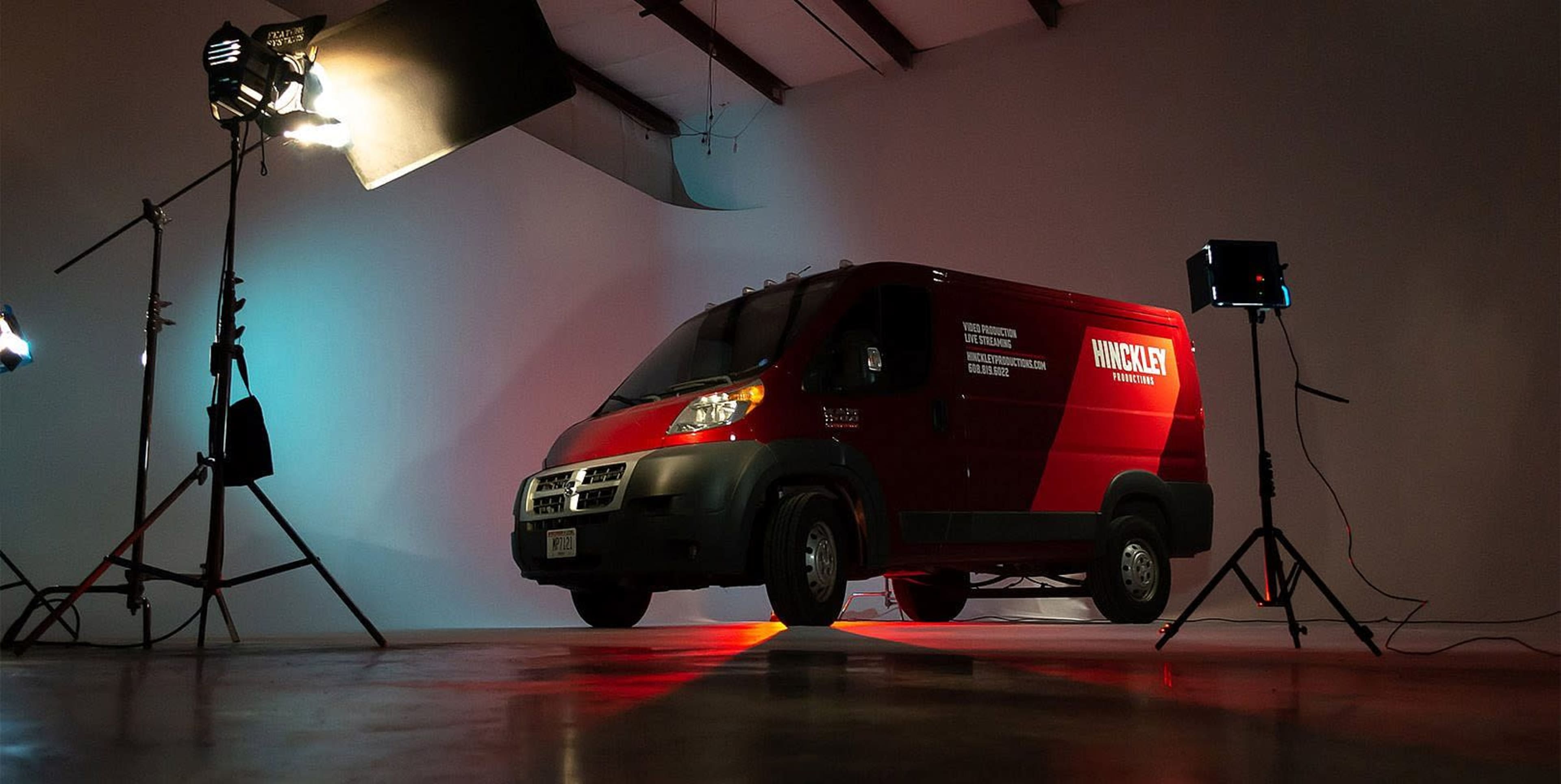 A red delivery van is positioned in a studio setting with professional lighting equipment surrounding it.