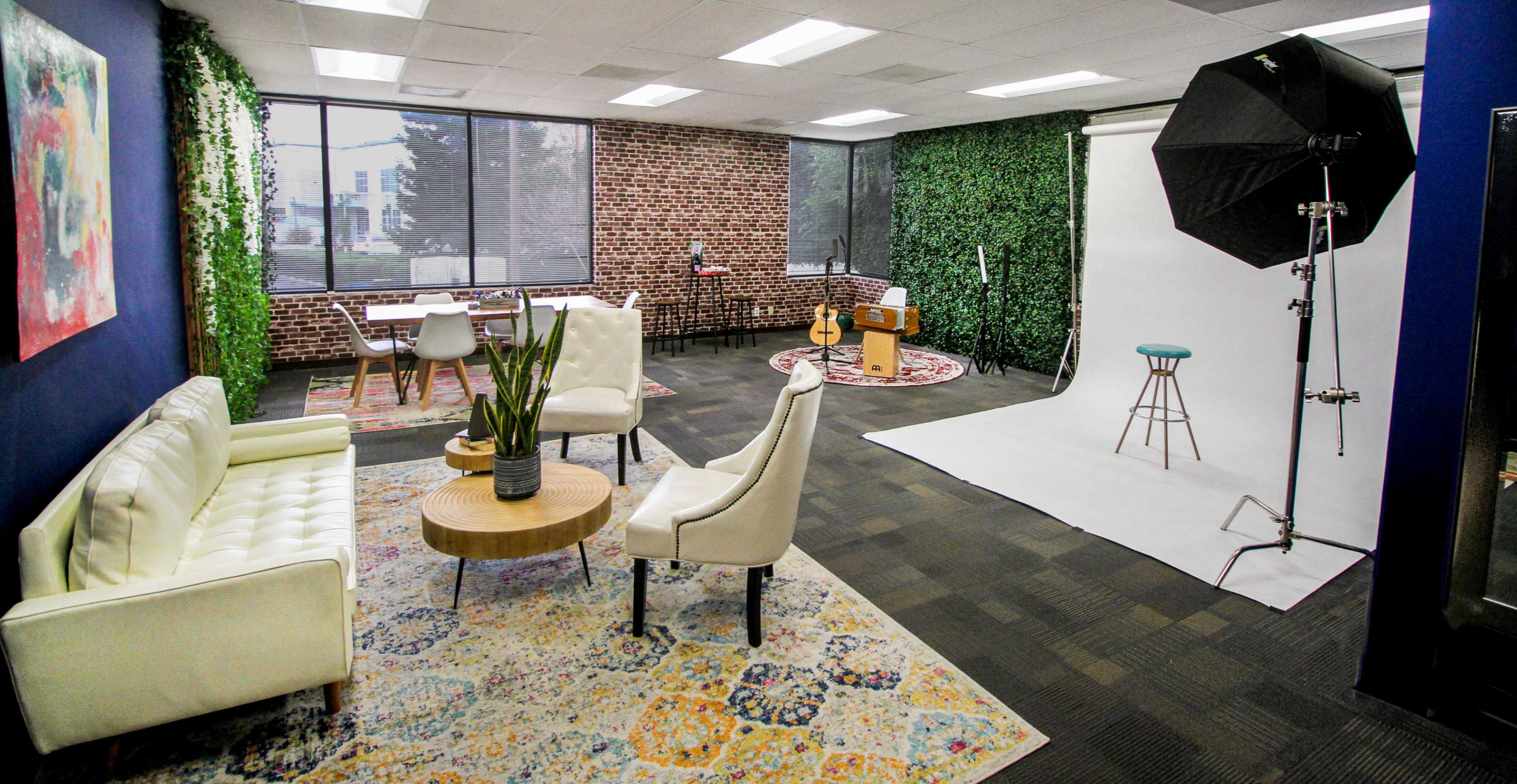 The image shows a modern studio with a seating area, a backdrop setup for photography, and green decorative elements on the walls.