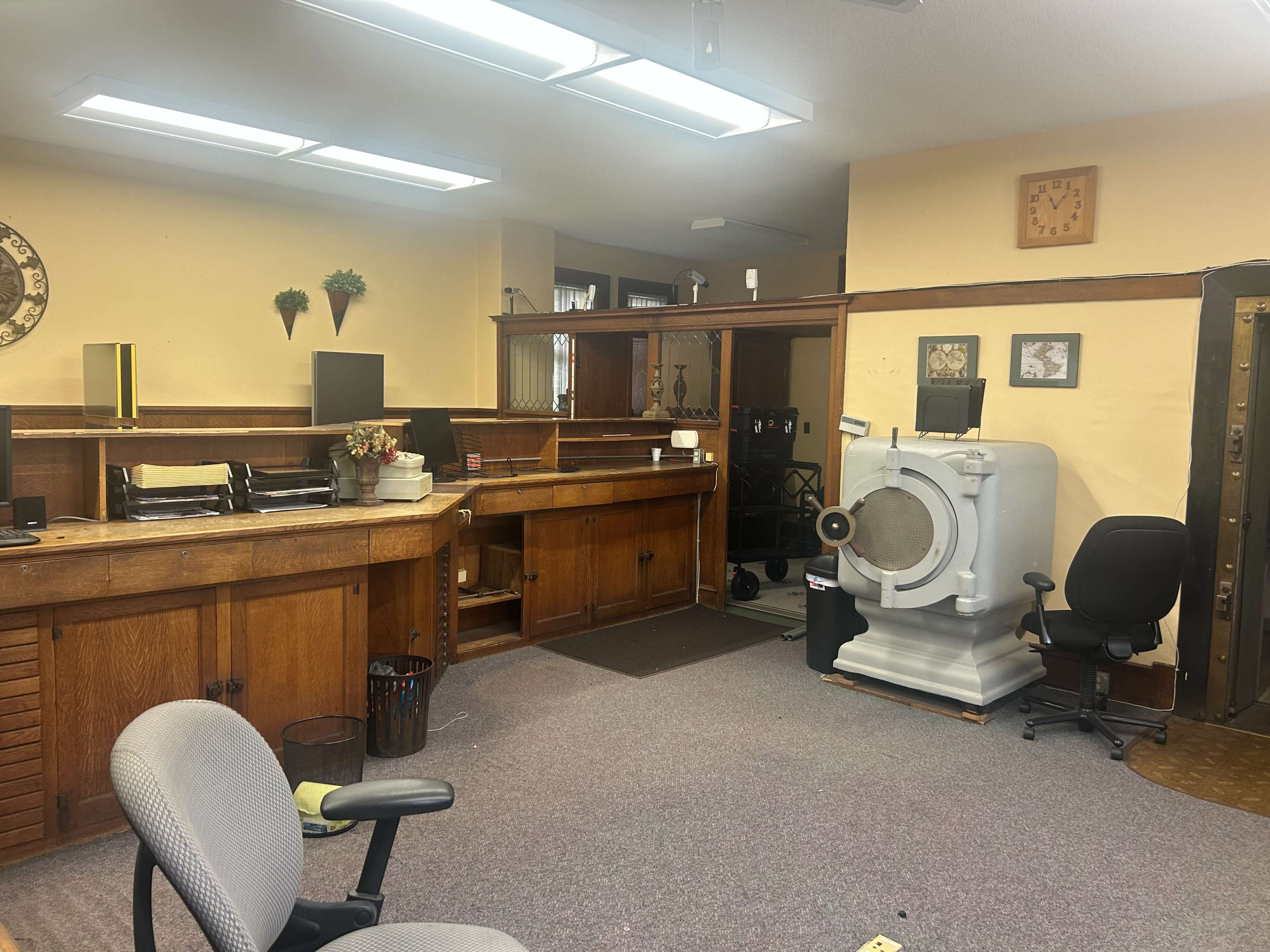 The image shows an office space with wooden cabinetry, a large safe, and two office chairs on a carpeted floor.