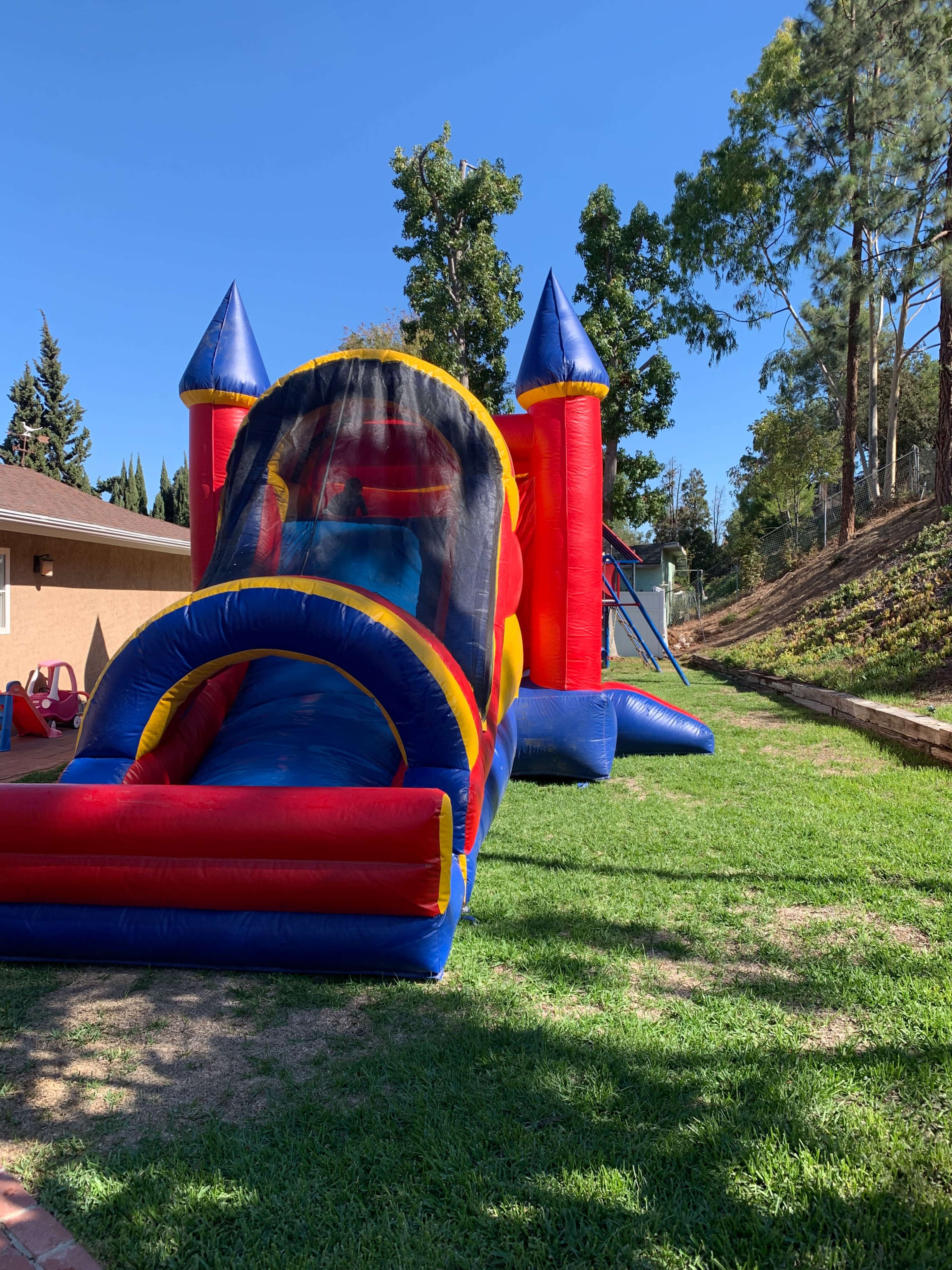 A colorful inflatable bounce house with a slide is set up on a grassy area beside a house.