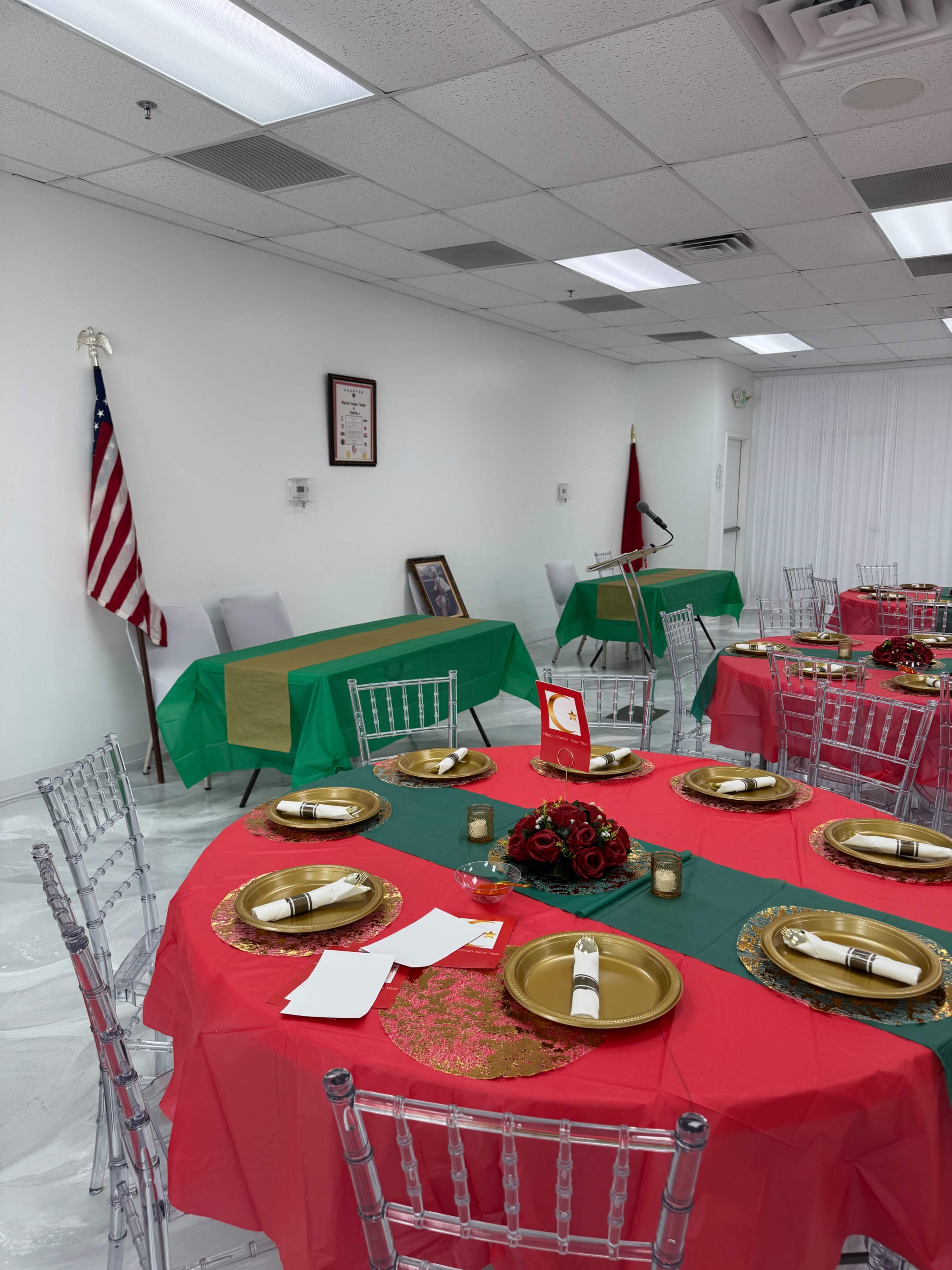 The image shows a decorated event space with tables covered in red and green tablecloths, gold plates, and floral centerpieces, alongside a U.S. flag and other items on the wall.