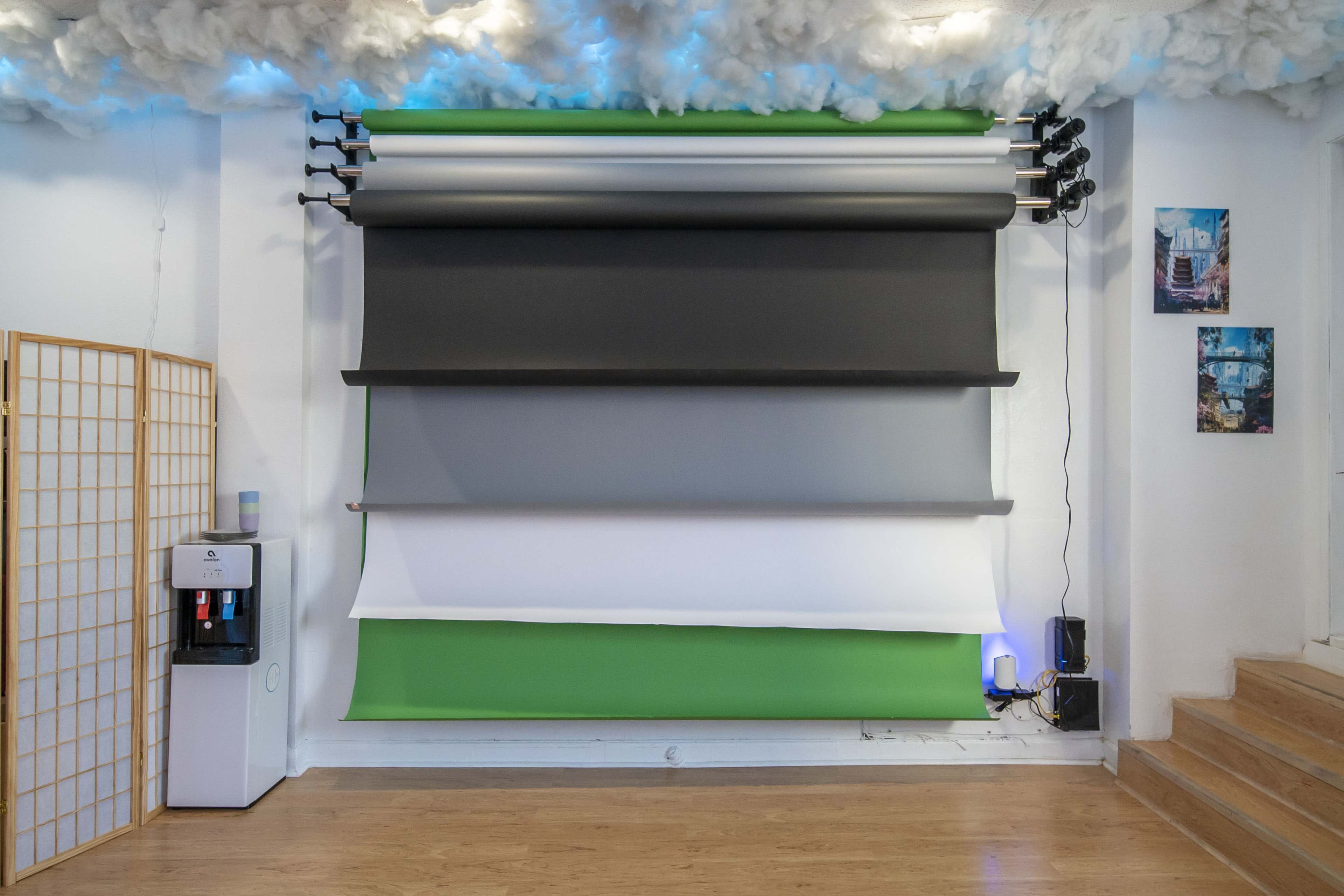 A wall with multiple rolled fabric backdrops in gray, white, and green, alongside a water cooler and framed pictures.