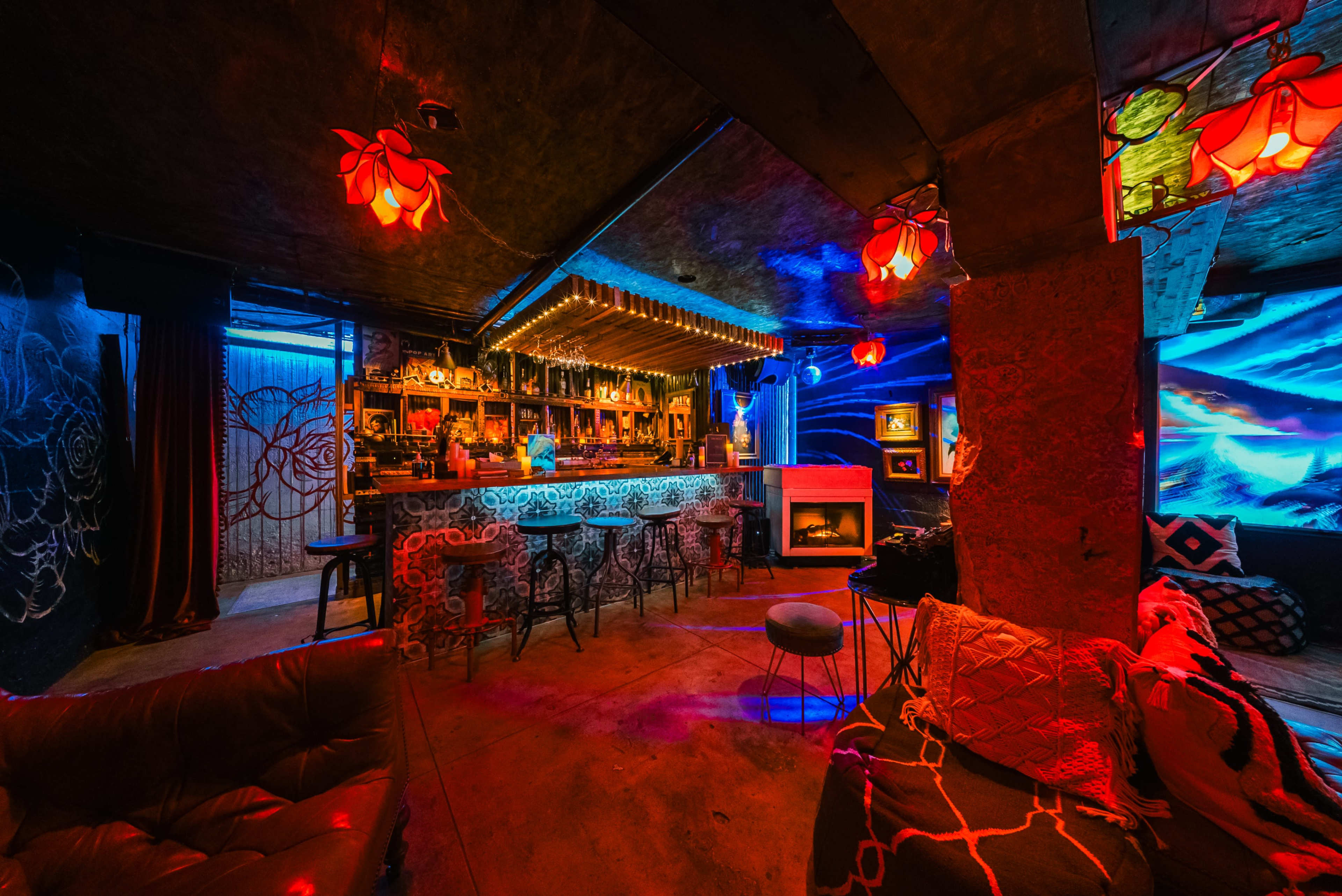 The image shows an interior of a bar featuring colorful lights, a long bar counter, and various seating areas with decorative elements.