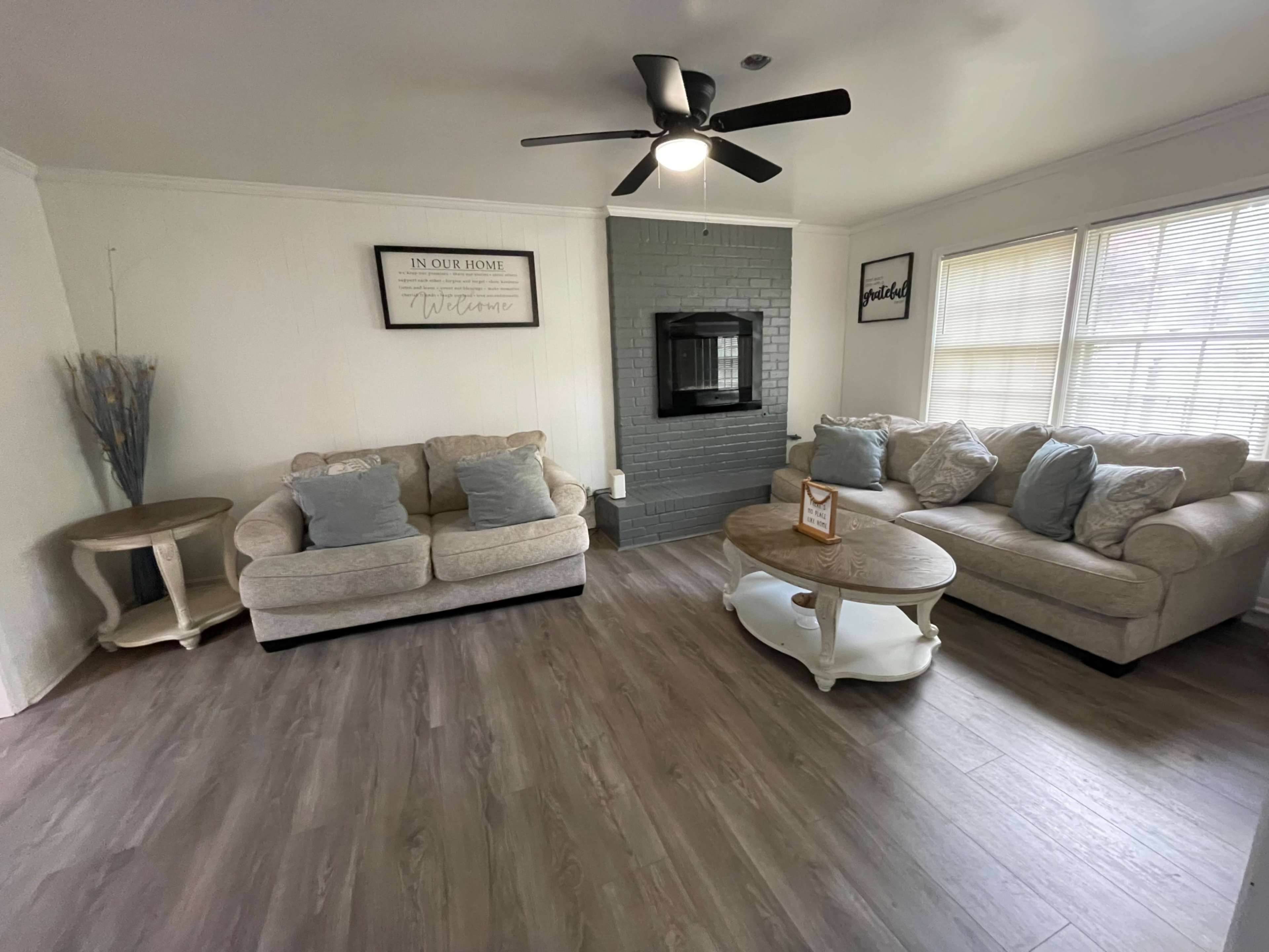 The living room features two light-colored sofas, a coffee table, and a fireplace with a decorative mantle.