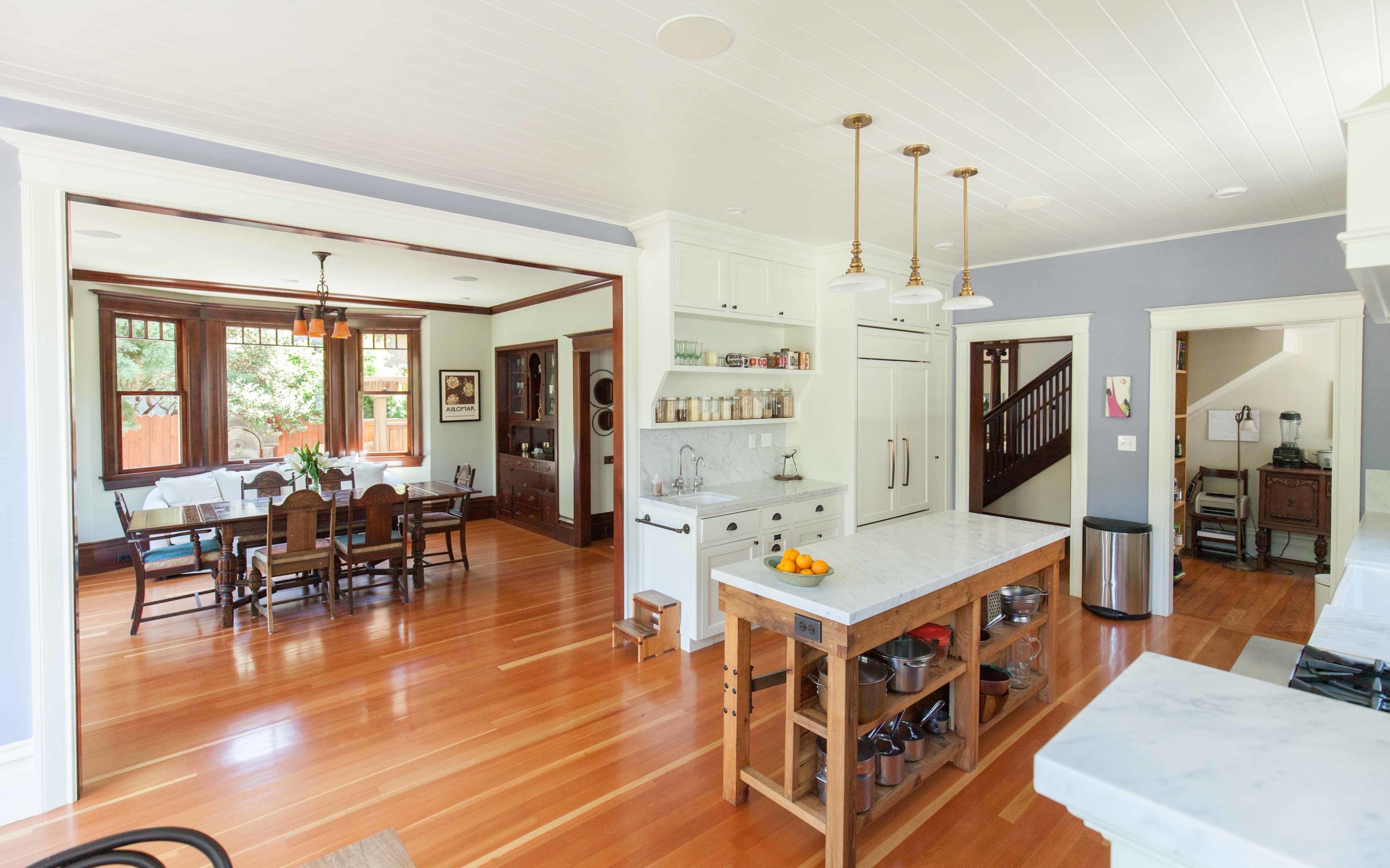 A spacious kitchen features a central island with a marble top and wooden base, leading to an adjoining dining area with a large table and chairs.