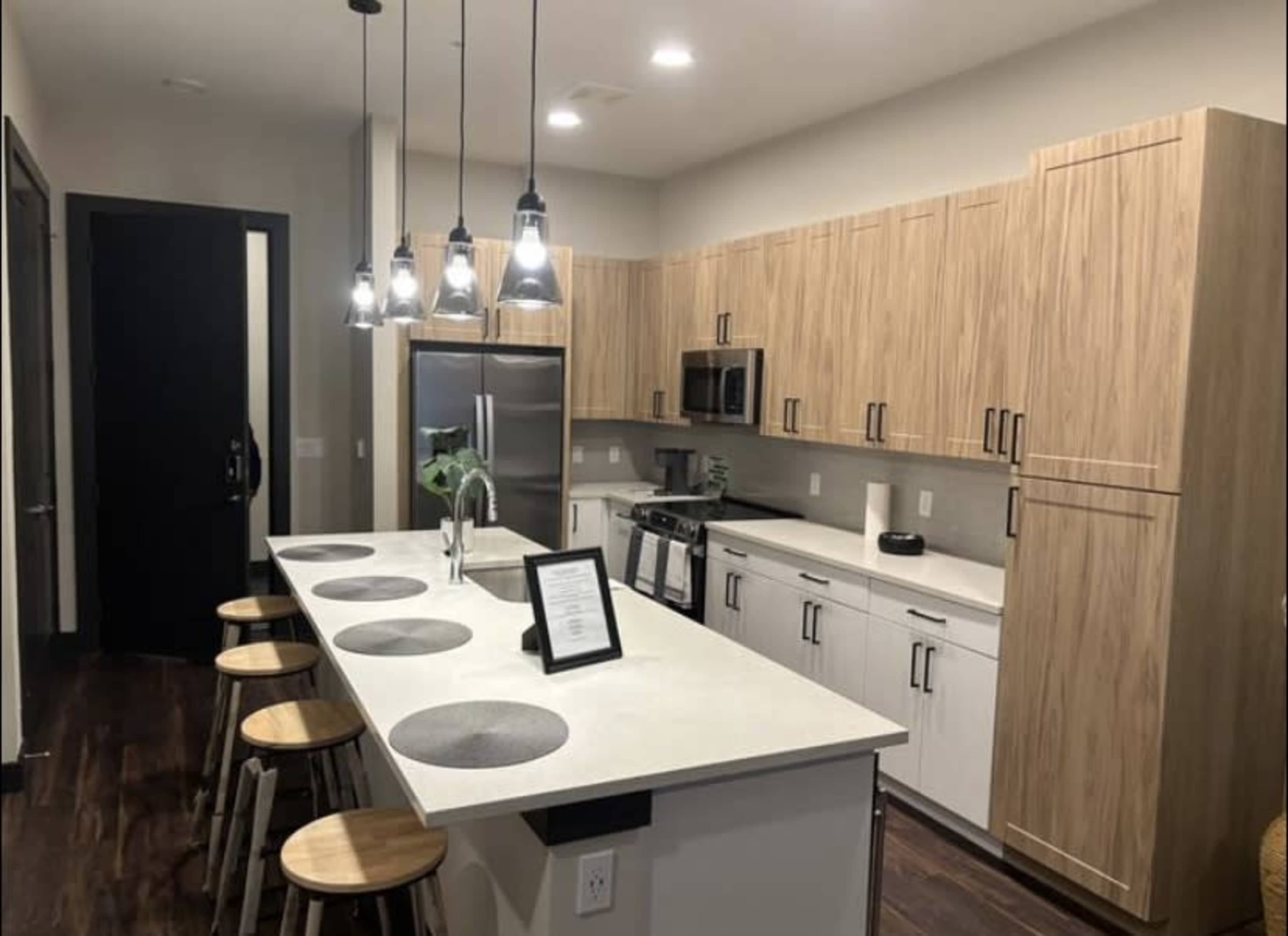 The image shows a modern kitchen with wooden cabinets, stainless steel appliances, and a central island with seating for four.