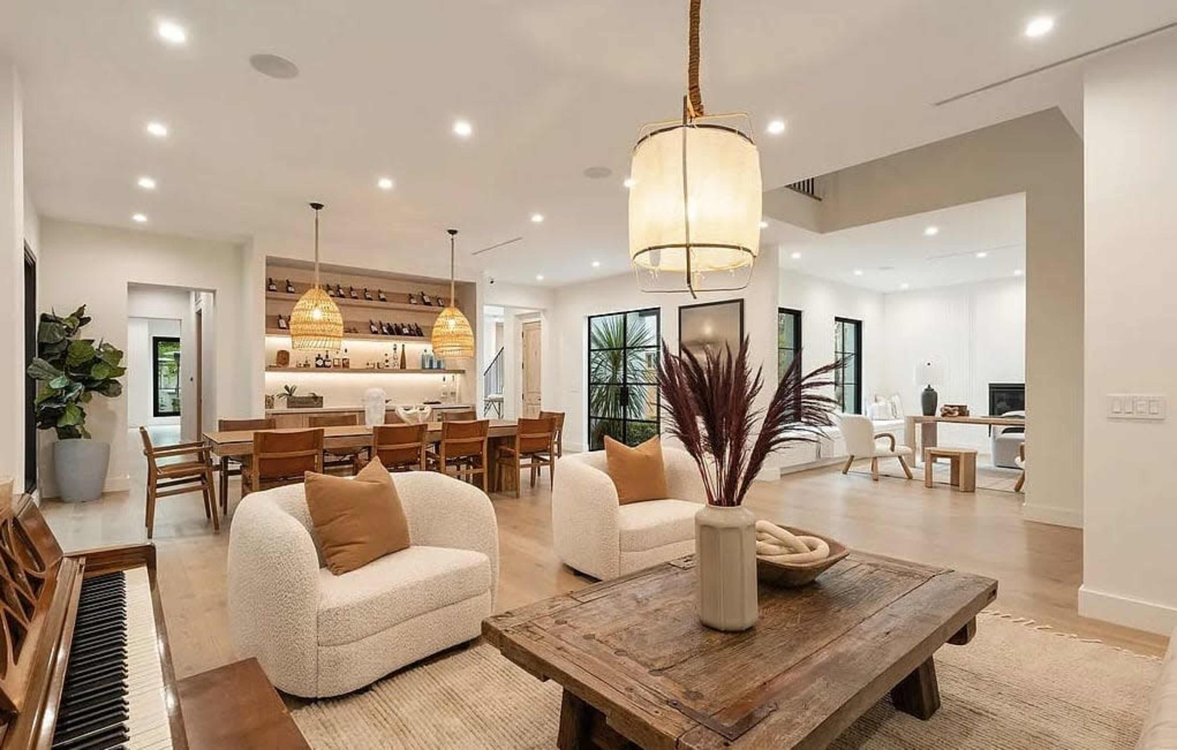 The image shows a modern open-concept living space with a dining area, a cozy seating arrangement, and a bar setup in the background.