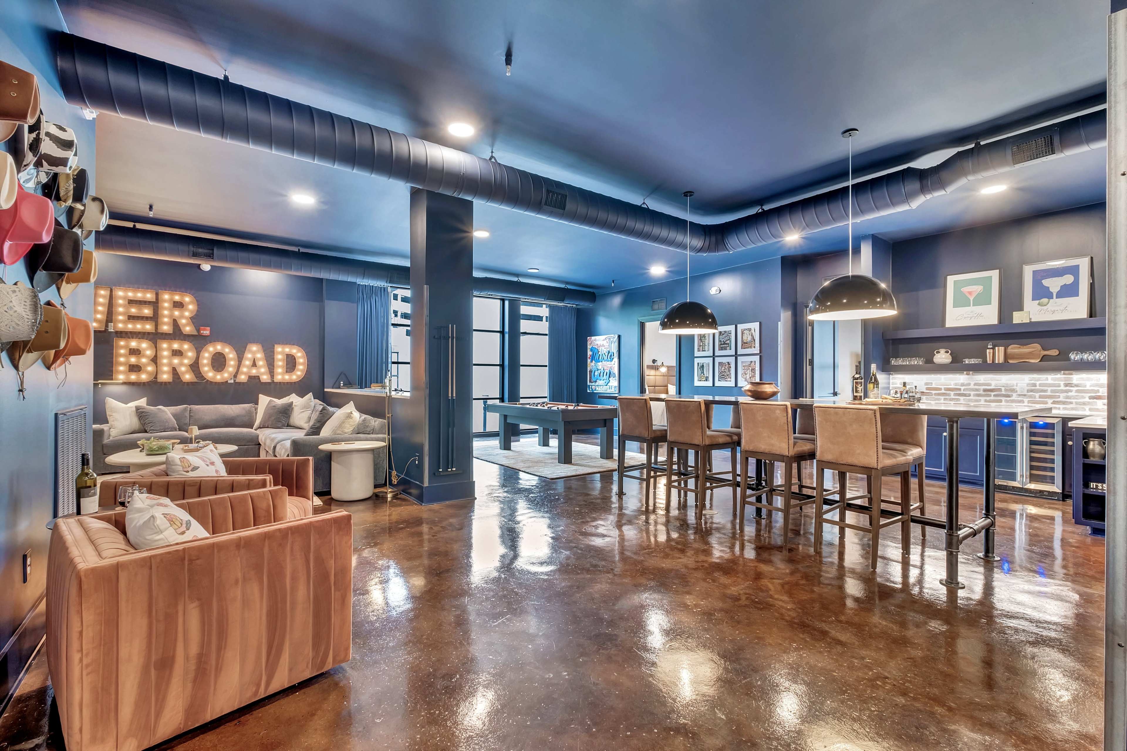 The image shows a stylish, modern lounge area with a pool table, a bar with seating, and decorative wall art.