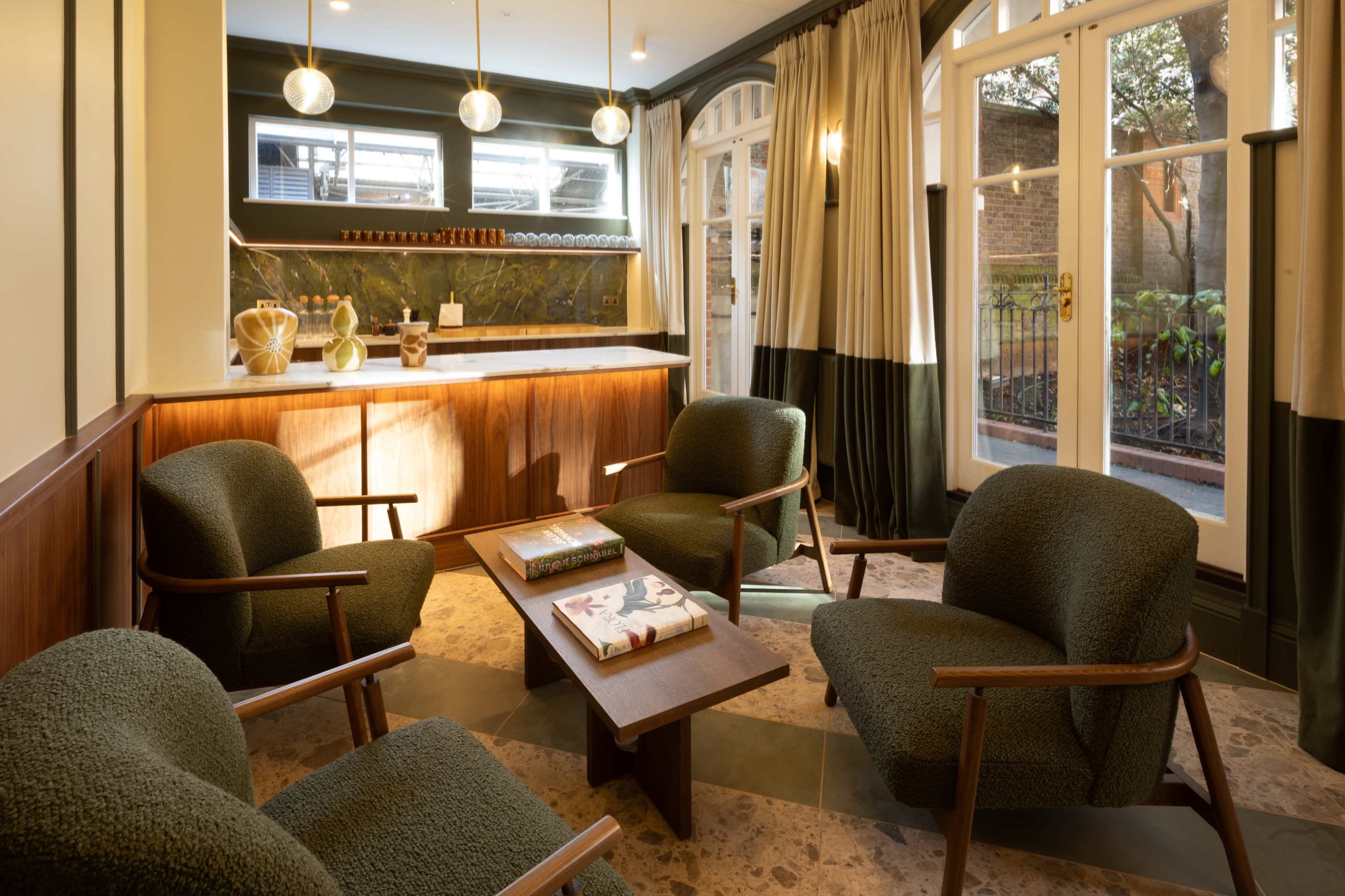 The image depicts a cozy seating area featuring four upholstered chairs surrounding a wooden coffee table in a well-lit room with large windows and warm wood accents.