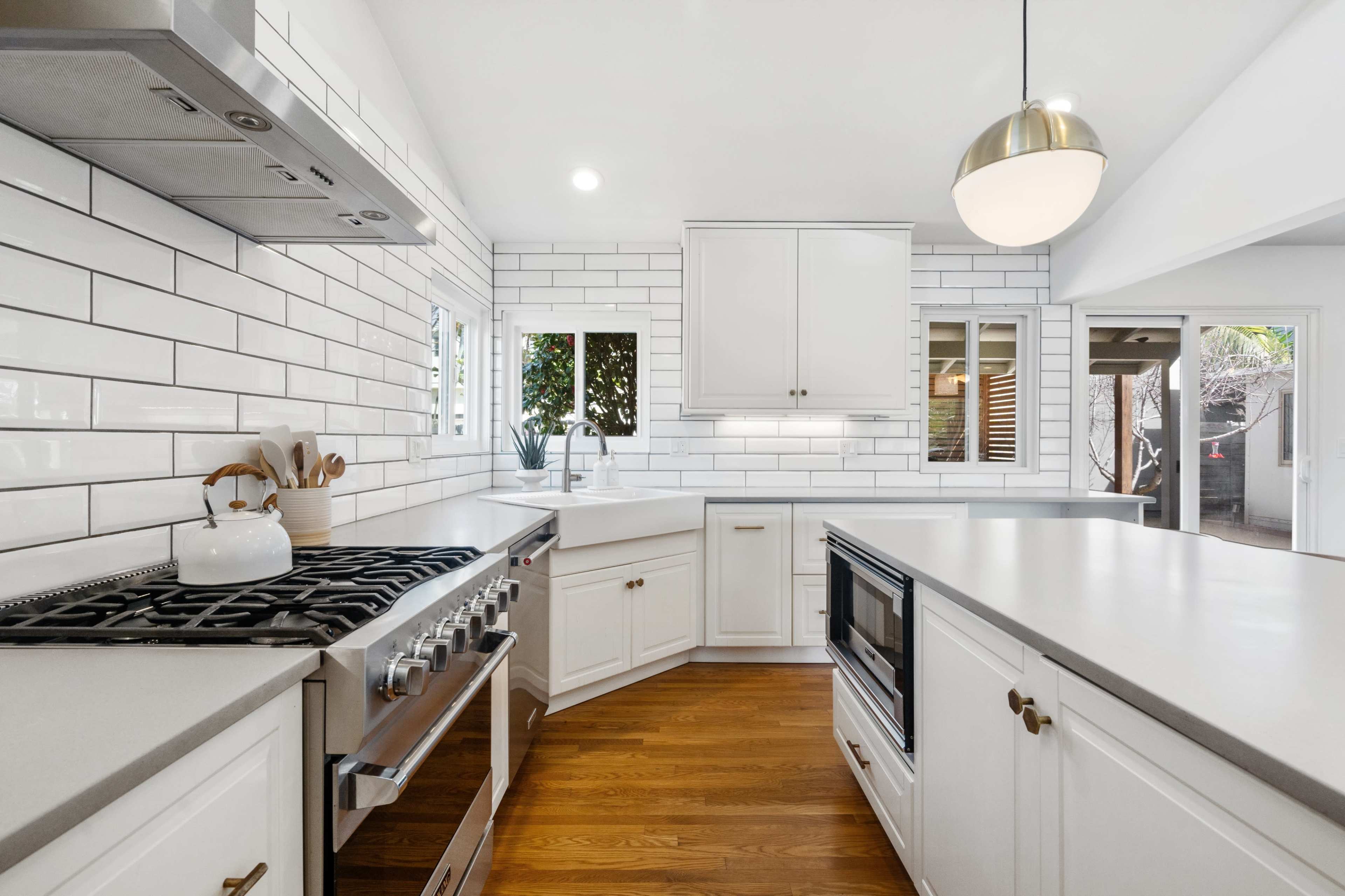 A bright kitchen features white tiled walls, a central island with a gray countertop, and stainless steel appliances, including a gas stove.
