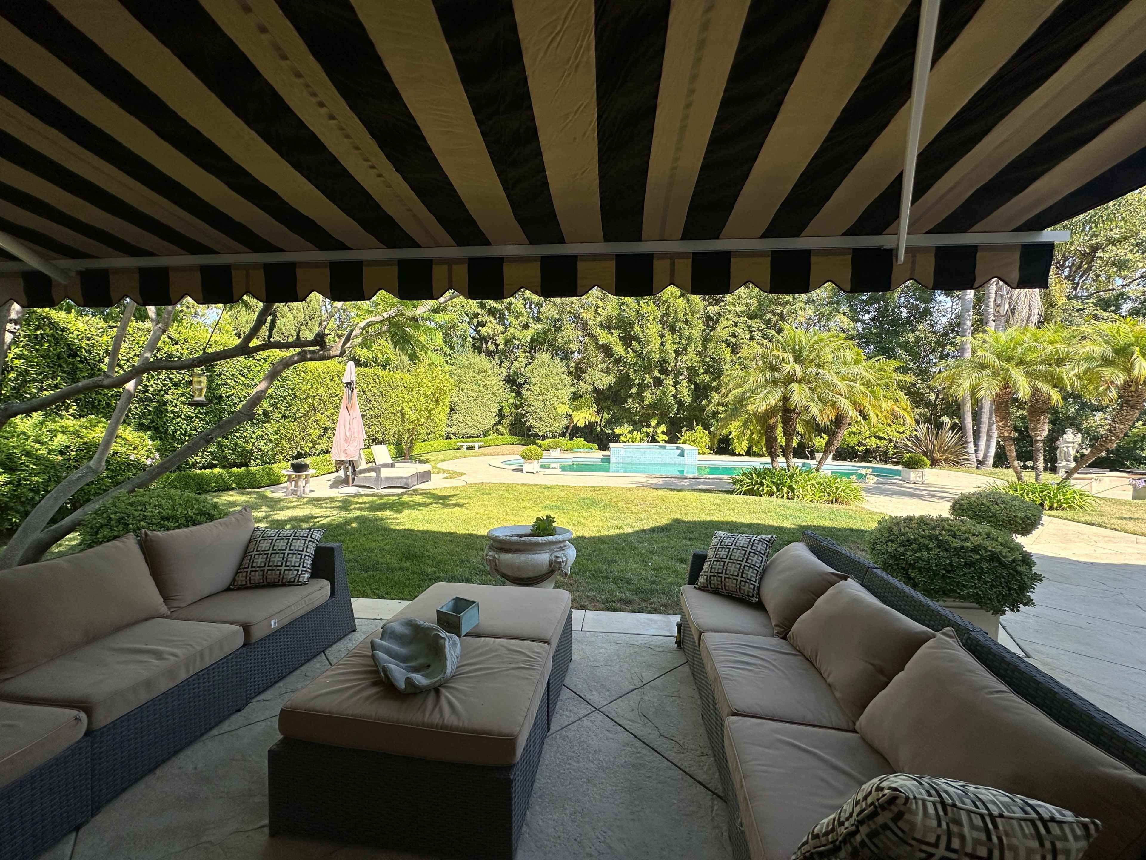 A patio area with comfortable seating and a view of a landscaped yard featuring a swimming pool and palm trees.