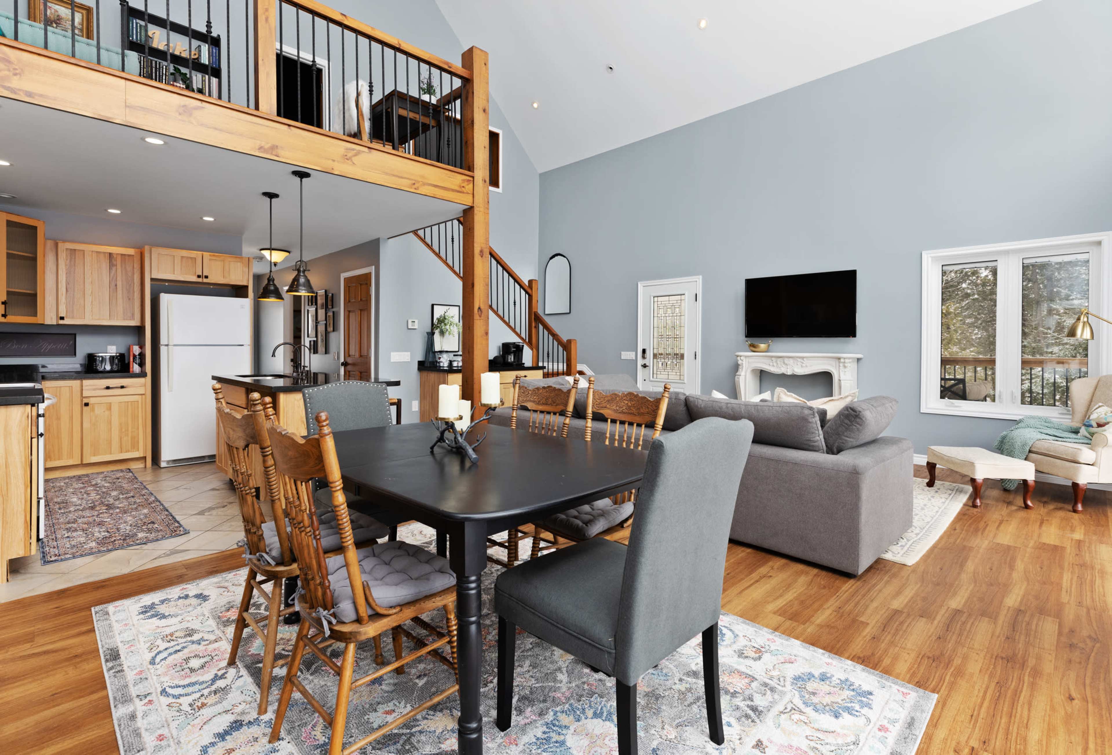 A spacious living area features a wooden dining table surrounded by chairs, a comfortable seating area with a couch, and large windows letting in natural light.