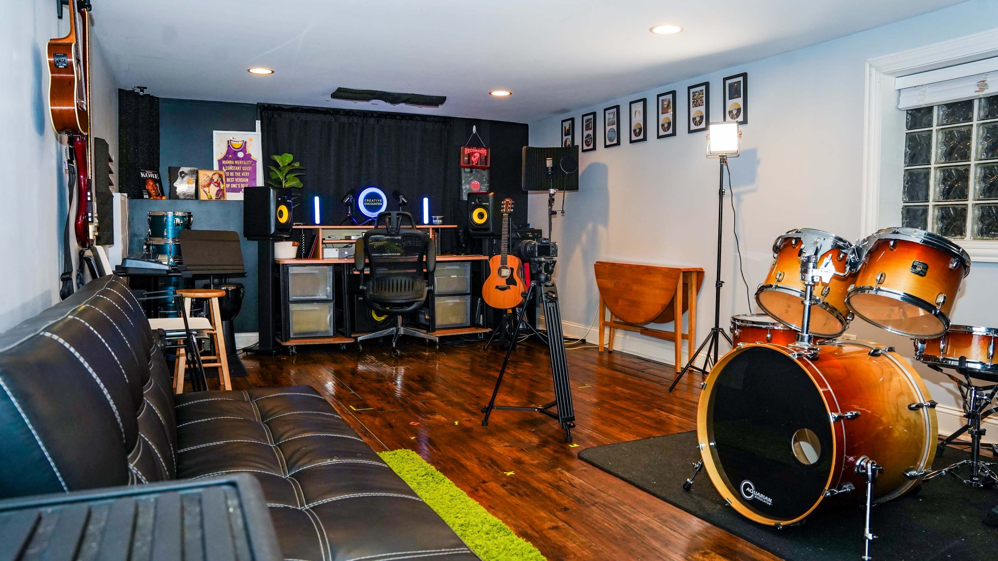 A home recording studio with guitars, a drum set, and a desk equipped with studio monitors and a microphone.