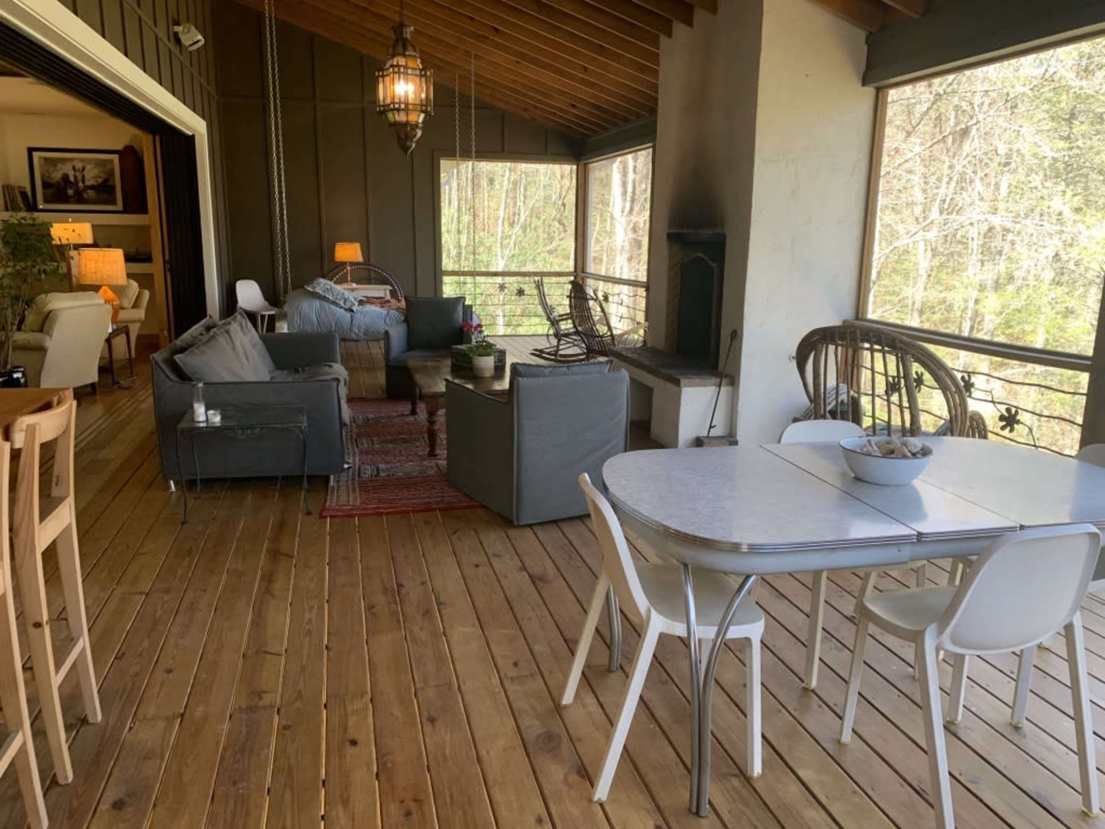 A spacious, open porch area with a dining table and seating arrangement overlooking a woodsy backdrop.