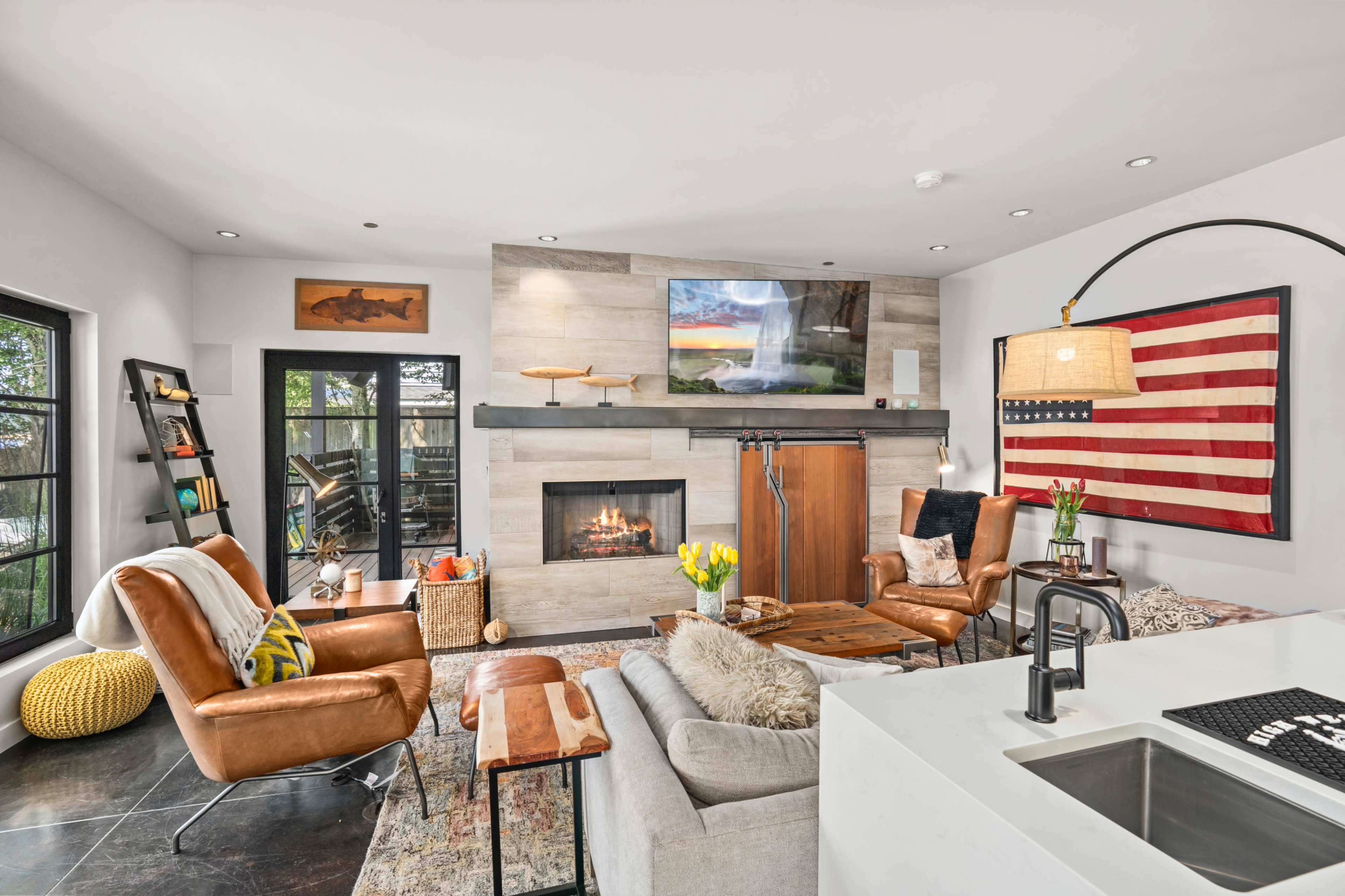 The living room features a modern design with a fireplace, wall-mounted television, leather seating, and large windows.