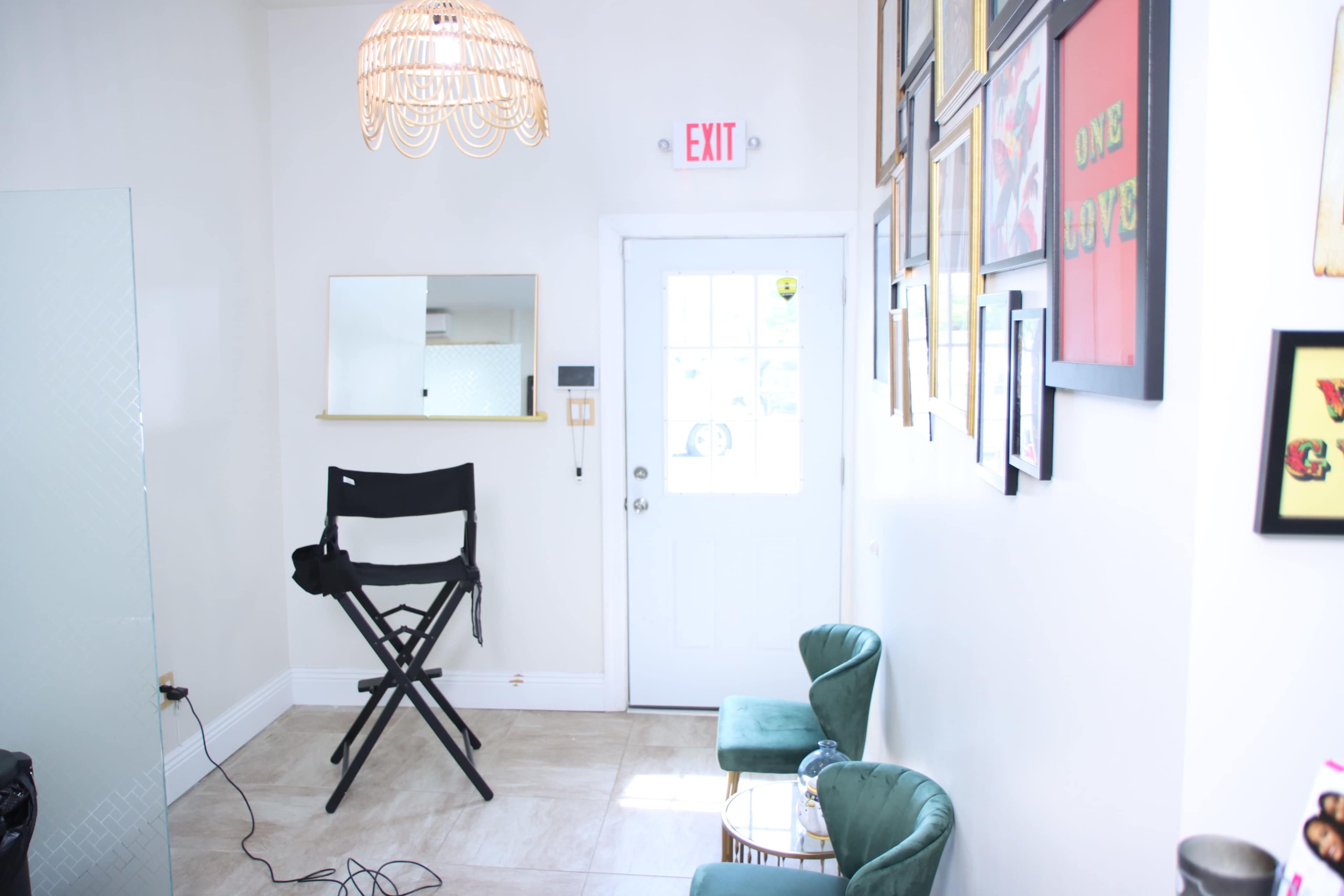 The room features a tall director's chair, a small round table, two green armchairs, and a door leading outside, with framed artwork hanging on the wall.