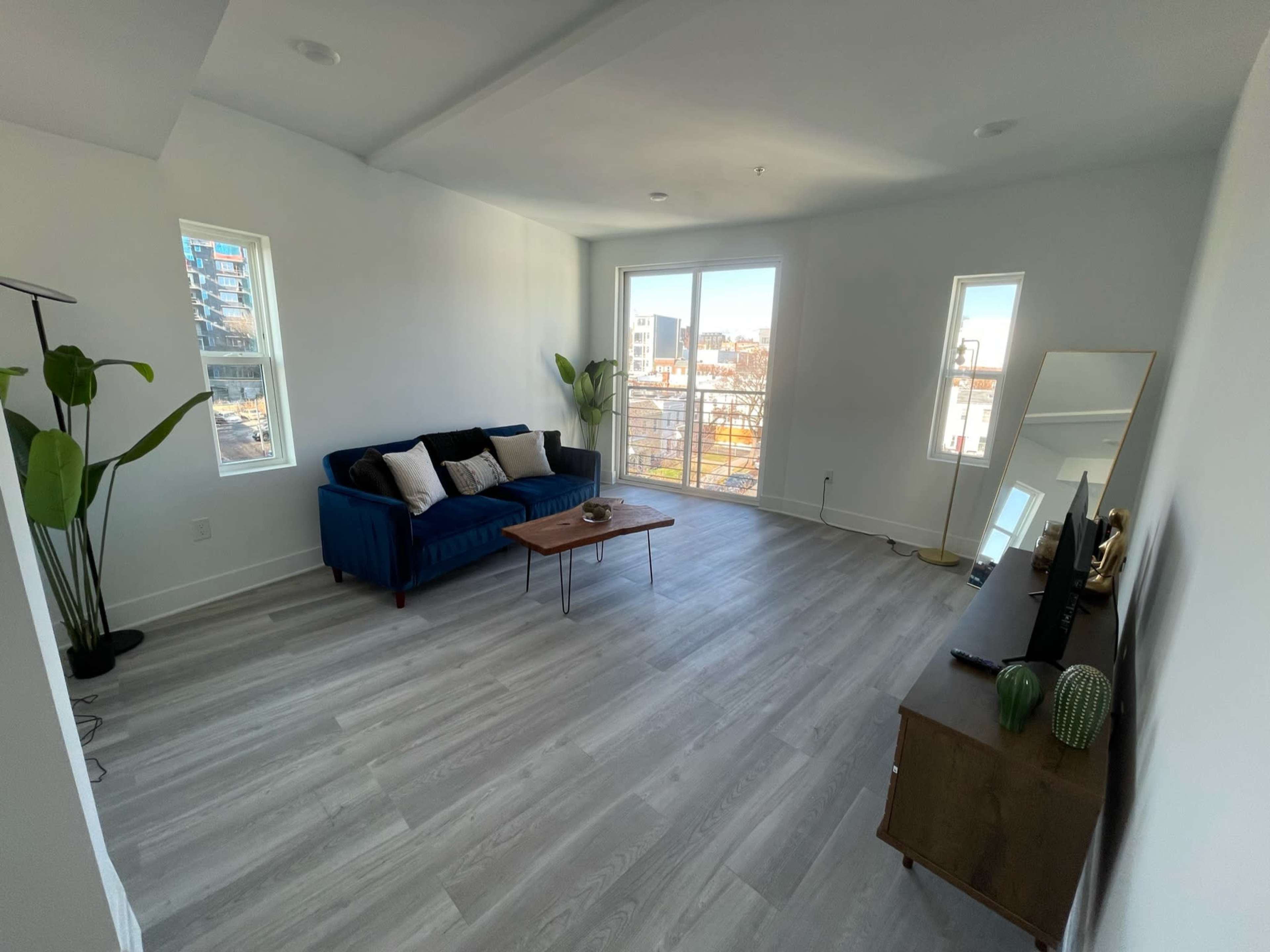 A bright and spacious living area featuring a blue sofa, a coffee table, and large windows with city views.