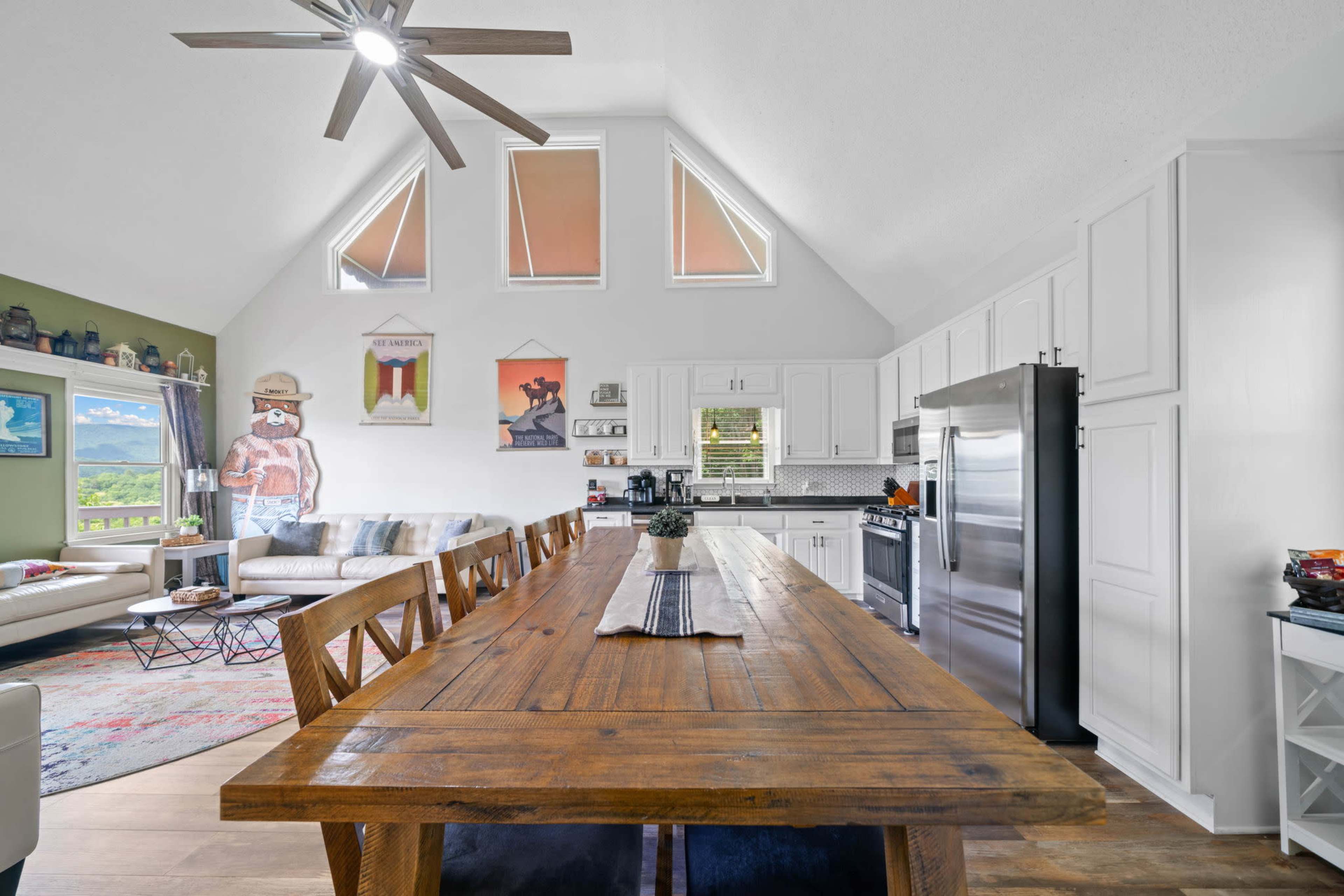 A spacious, modern kitchen and dining area features a large wooden table, stainless steel appliances, and tall windows with a scenic view.