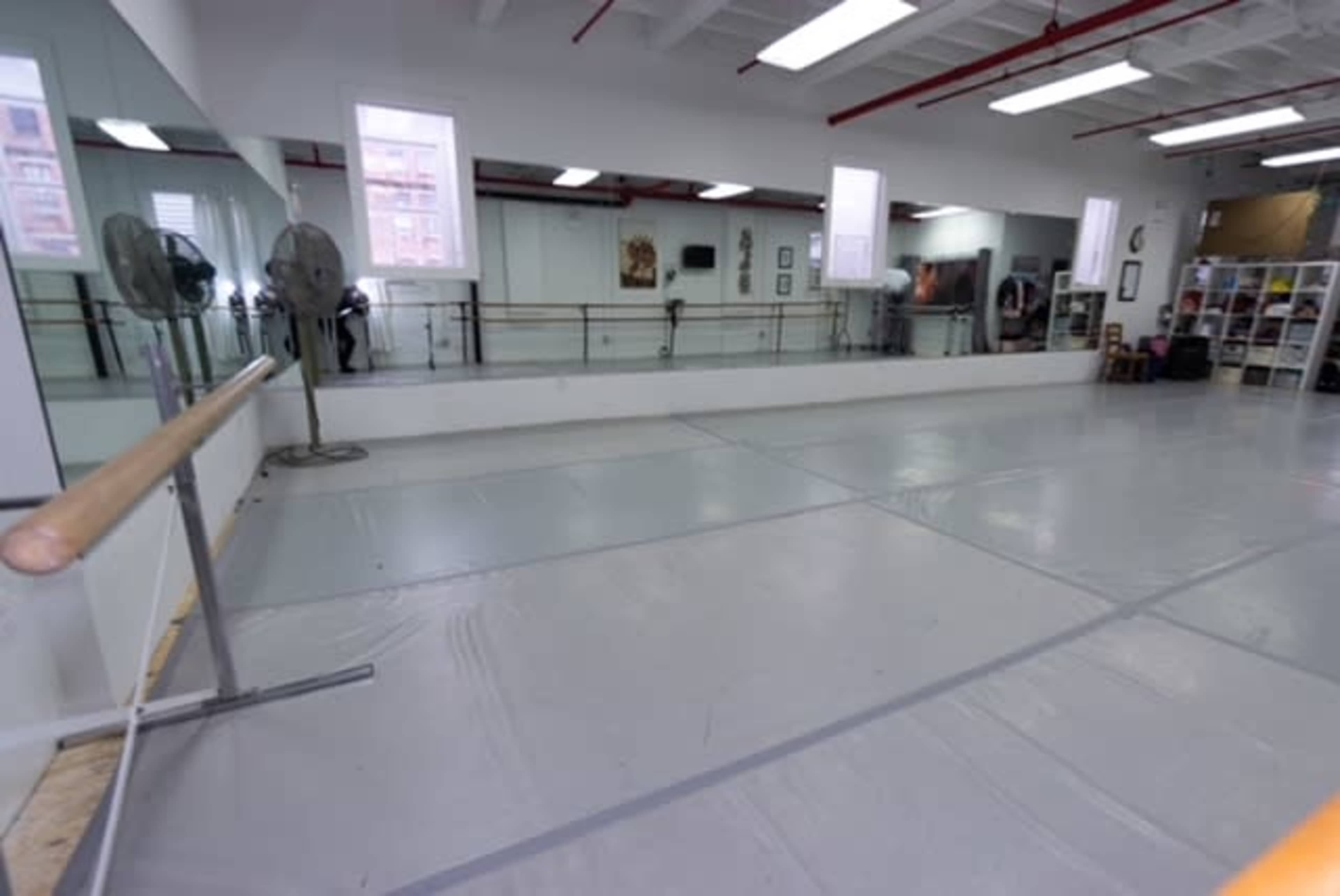 The image shows an empty dance studio with mirrored walls, a ballet bar, and a clear, lined floor.