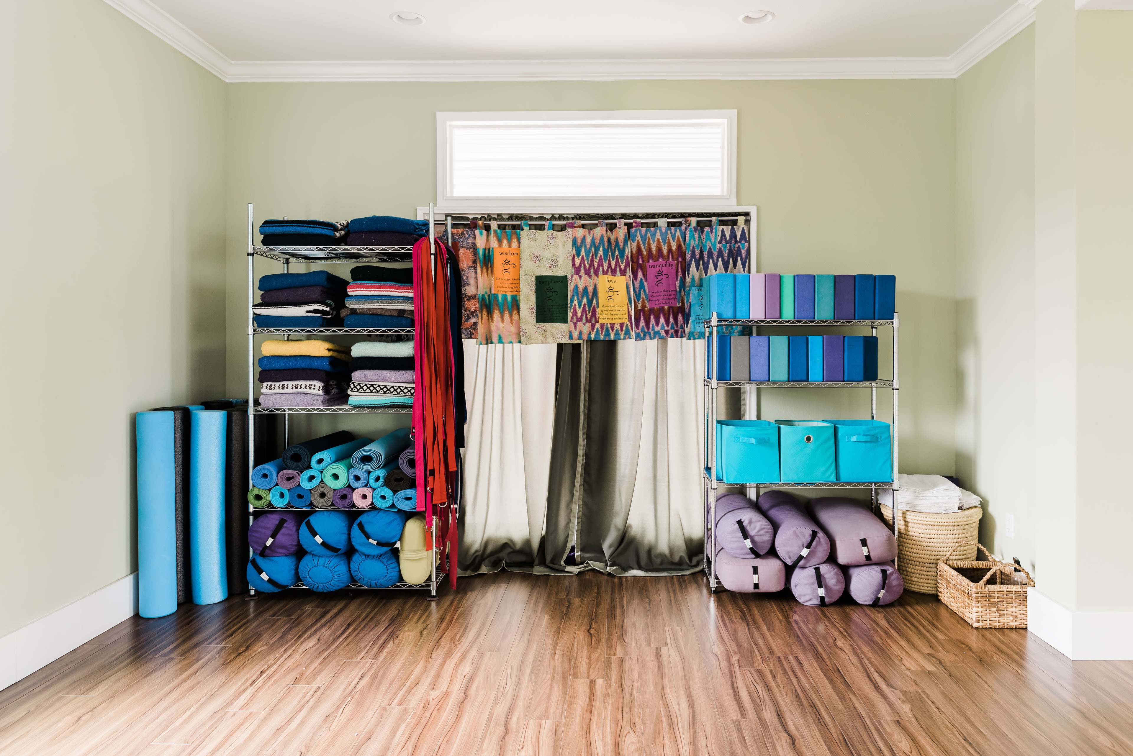 The image shows a neatly organized room featuring shelves filled with yoga mats, towels, and storage boxes, along with a curtain separating two sections.