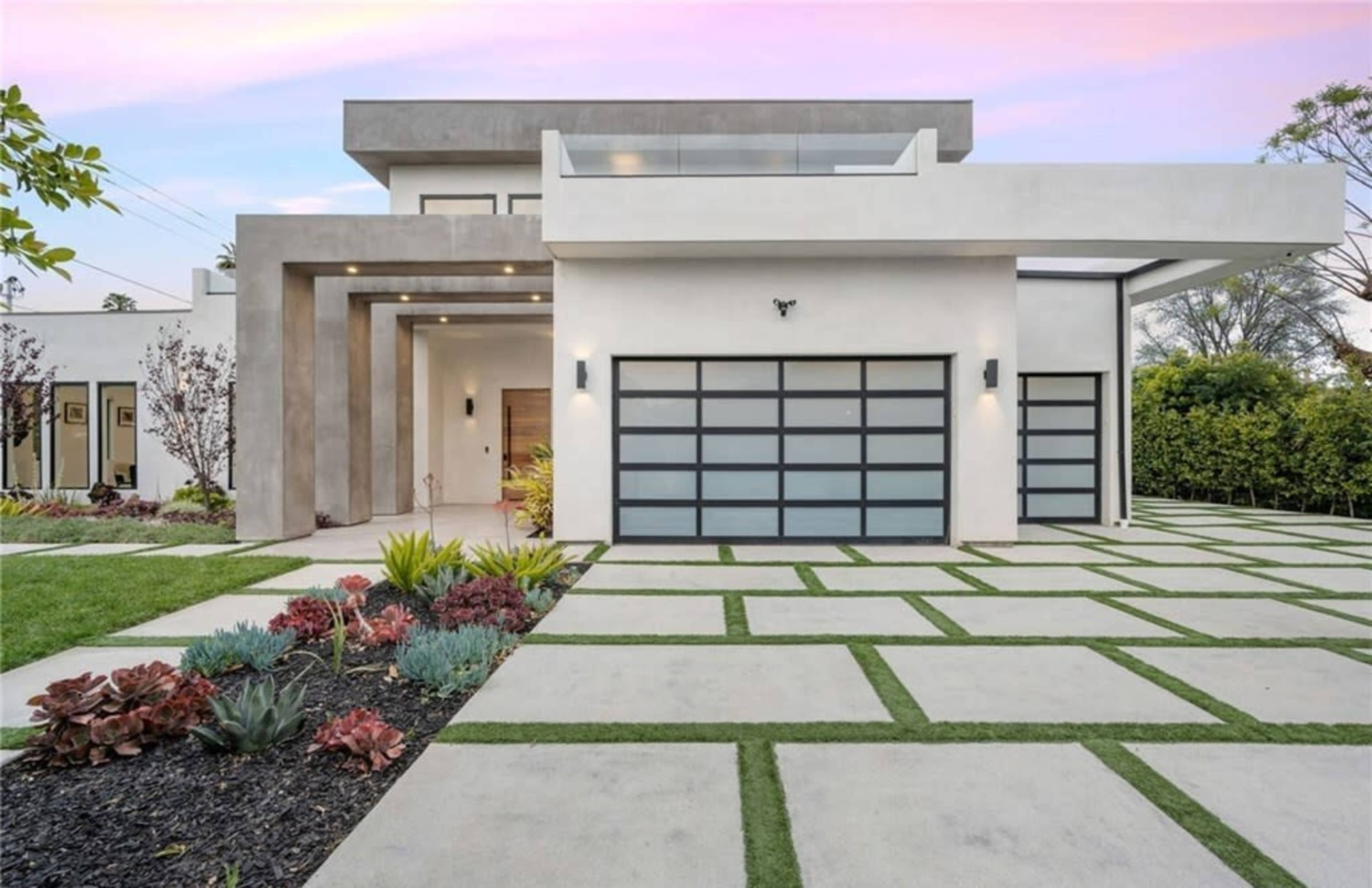 A modern house with a sleek exterior, featuring a large front yard and a driveway made of concrete with grass in between the slabs.