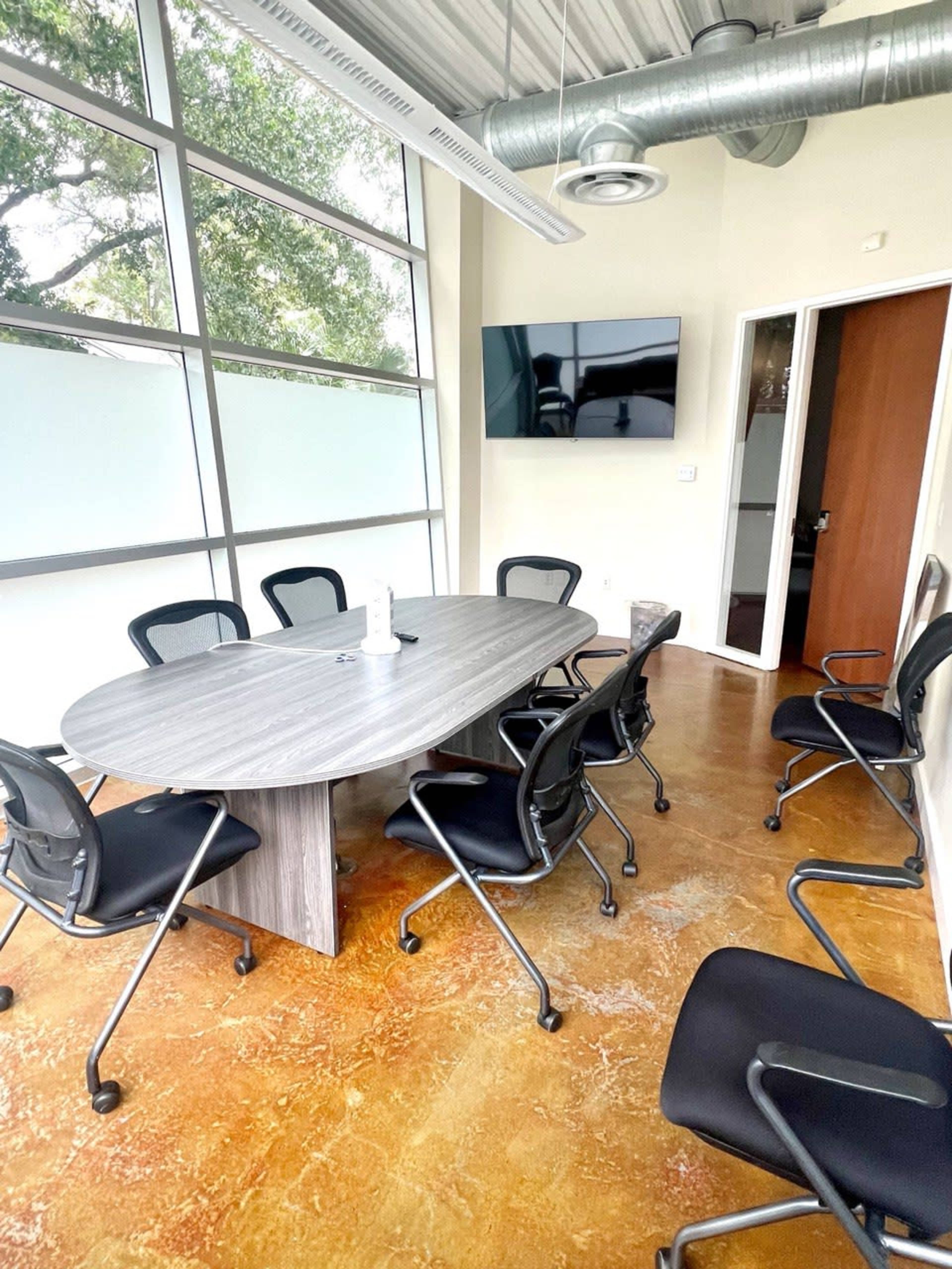 A conference room with a large oval table surrounded by black rolling chairs and a wall-mounted television.