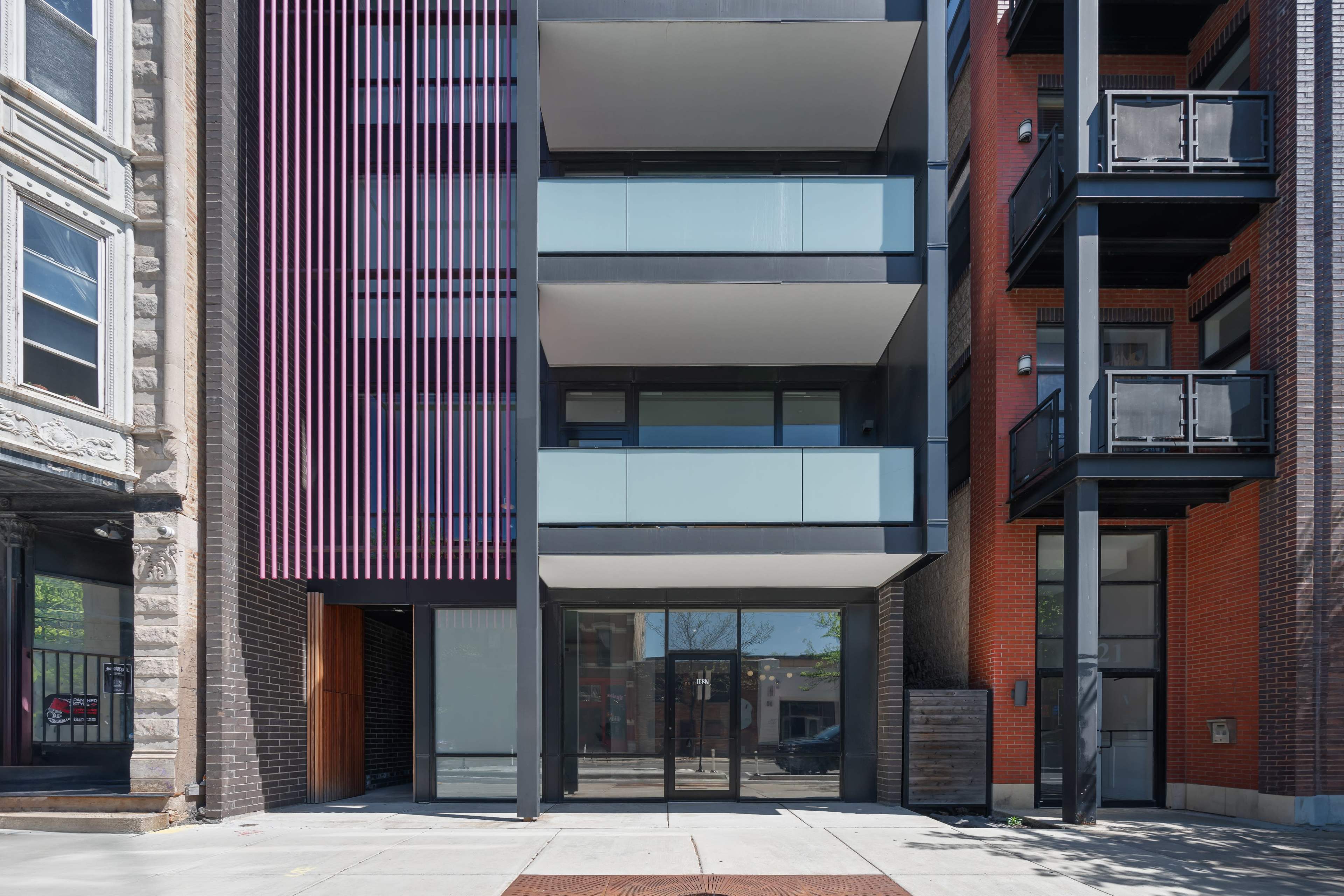 A modern building with glass balconies surrounded by older brick structures.