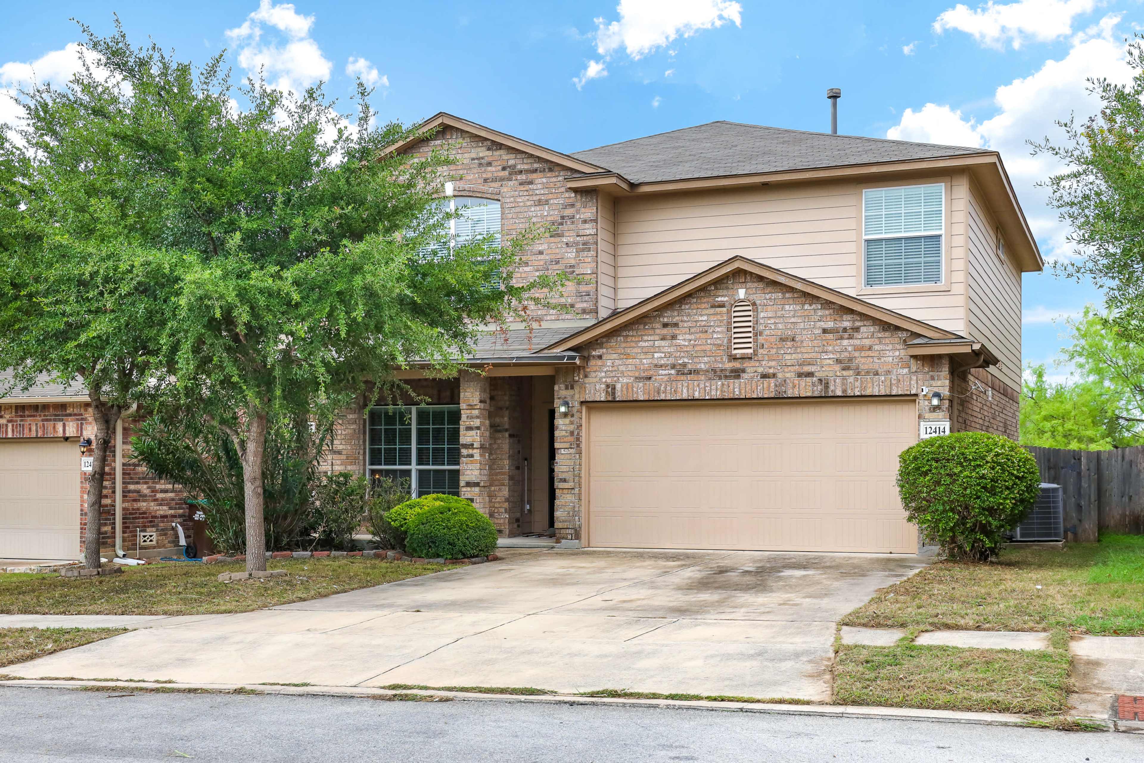 This two-story brick house features a well-maintained front yard and a double garage on a residential street.