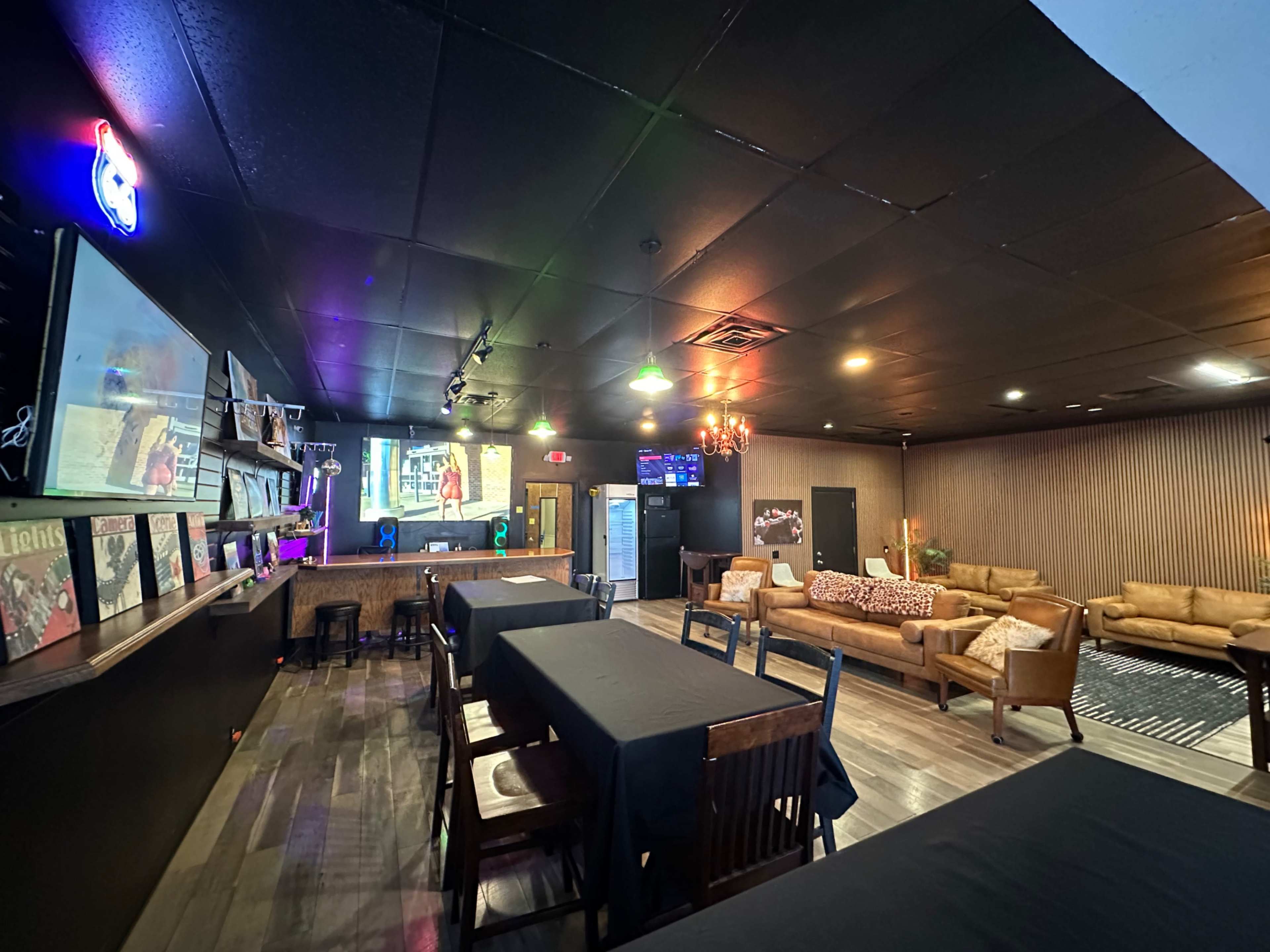 The image shows a colorful lounge area with multiple seating options, a large screen displaying a video, and a wall decorated with records.