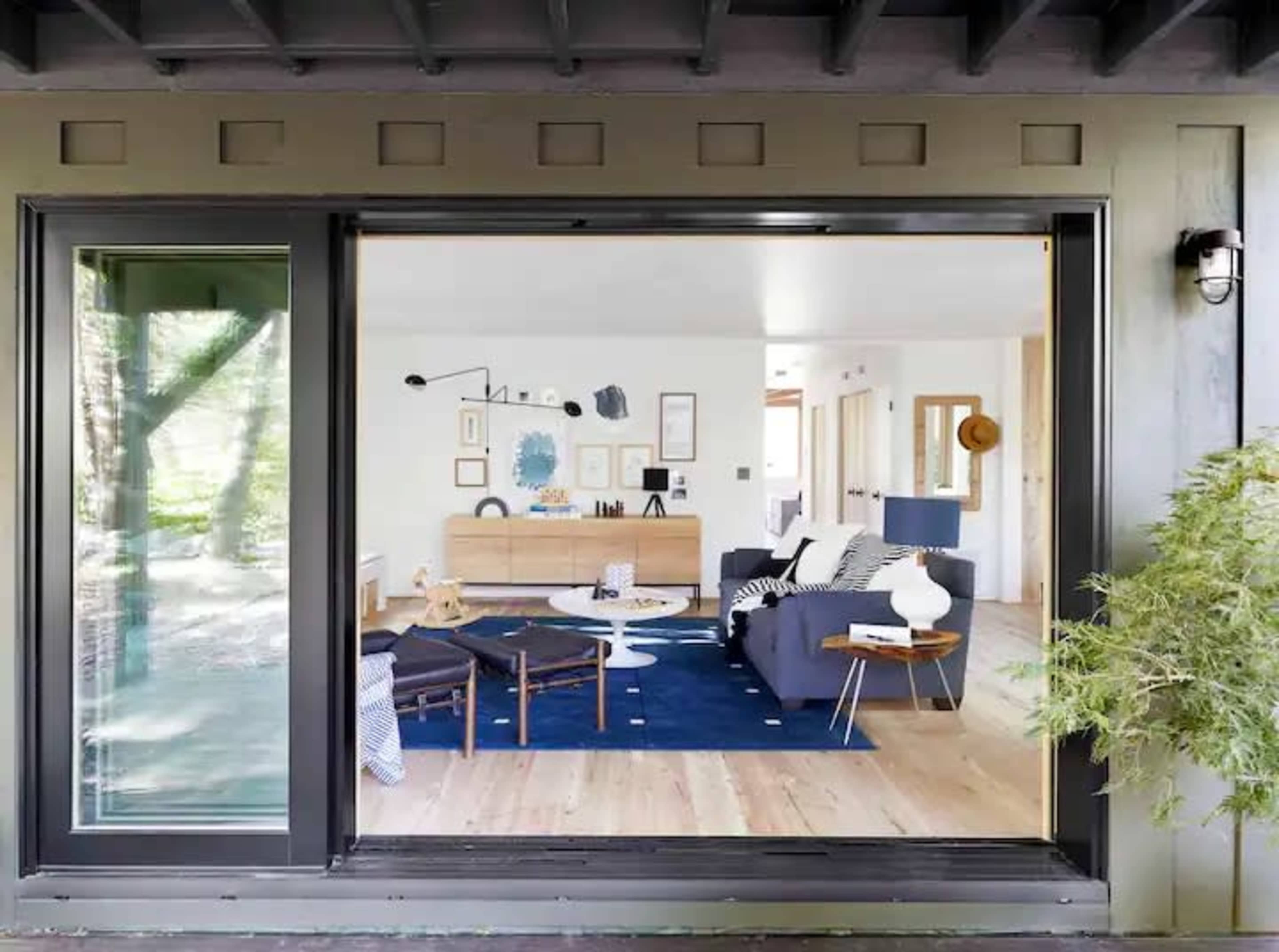 A modern living room with minimal furniture, framed artwork, and large windows is visible through an open sliding door.