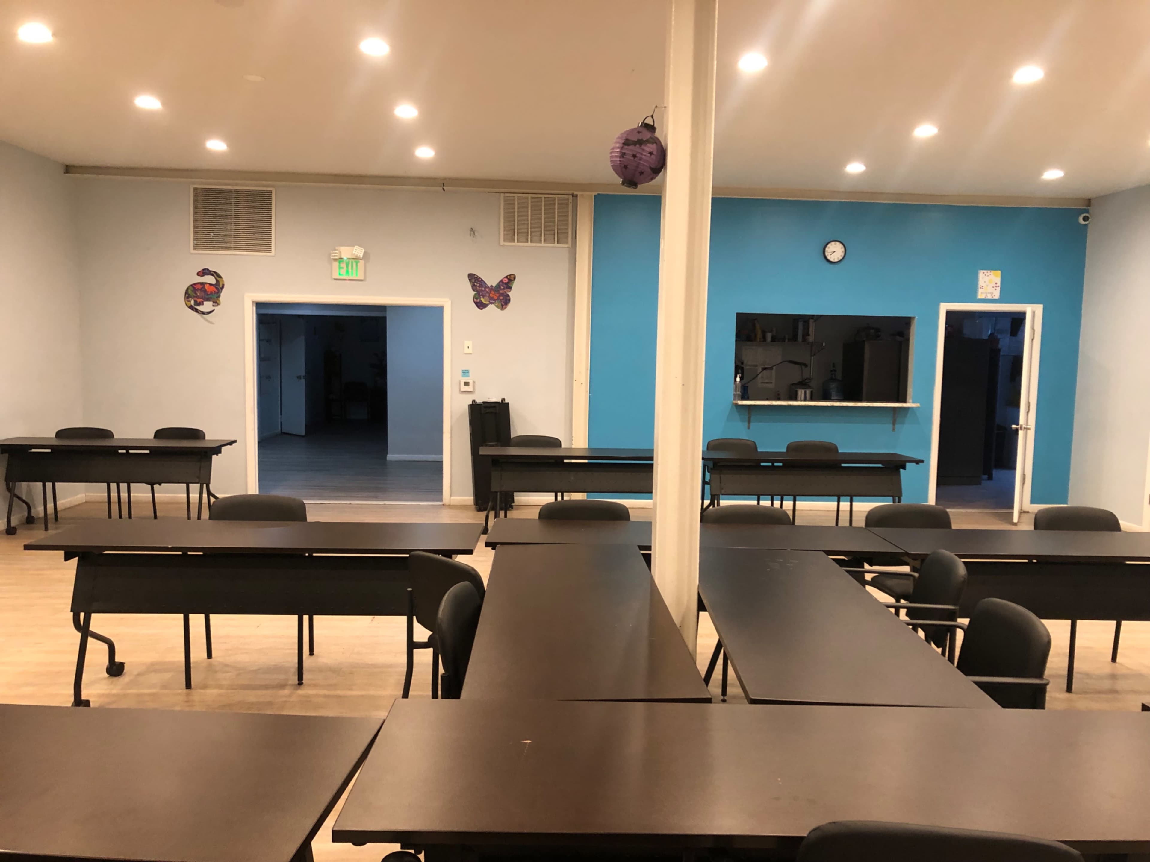 A classroom setup with multiple black tables and chairs arranged in a spacious room, featuring light blue walls and decorative butterflies.