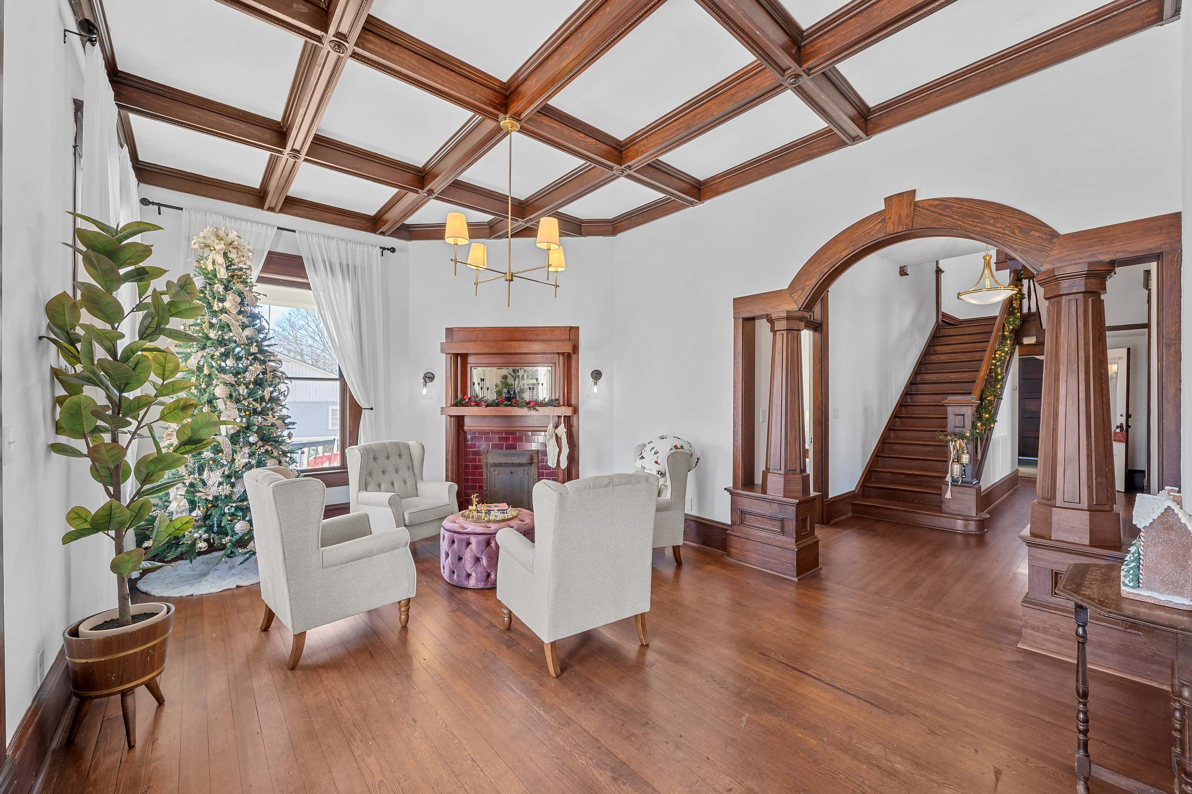 A living room features two armchairs, a round table, a Christmas tree, and a staircase that leads to another level.