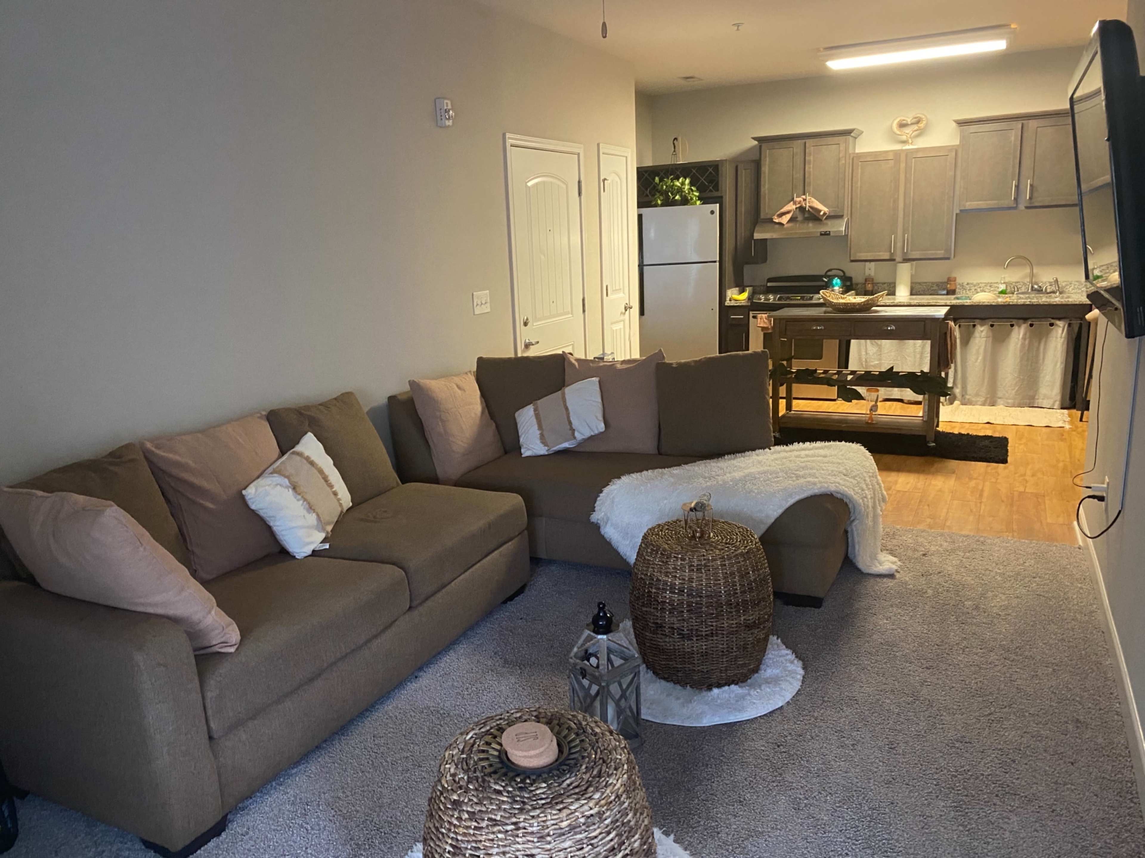The living room features a sectional sofa, a coffee table, and a view of a kitchen with gray cabinets and a refrigerator.