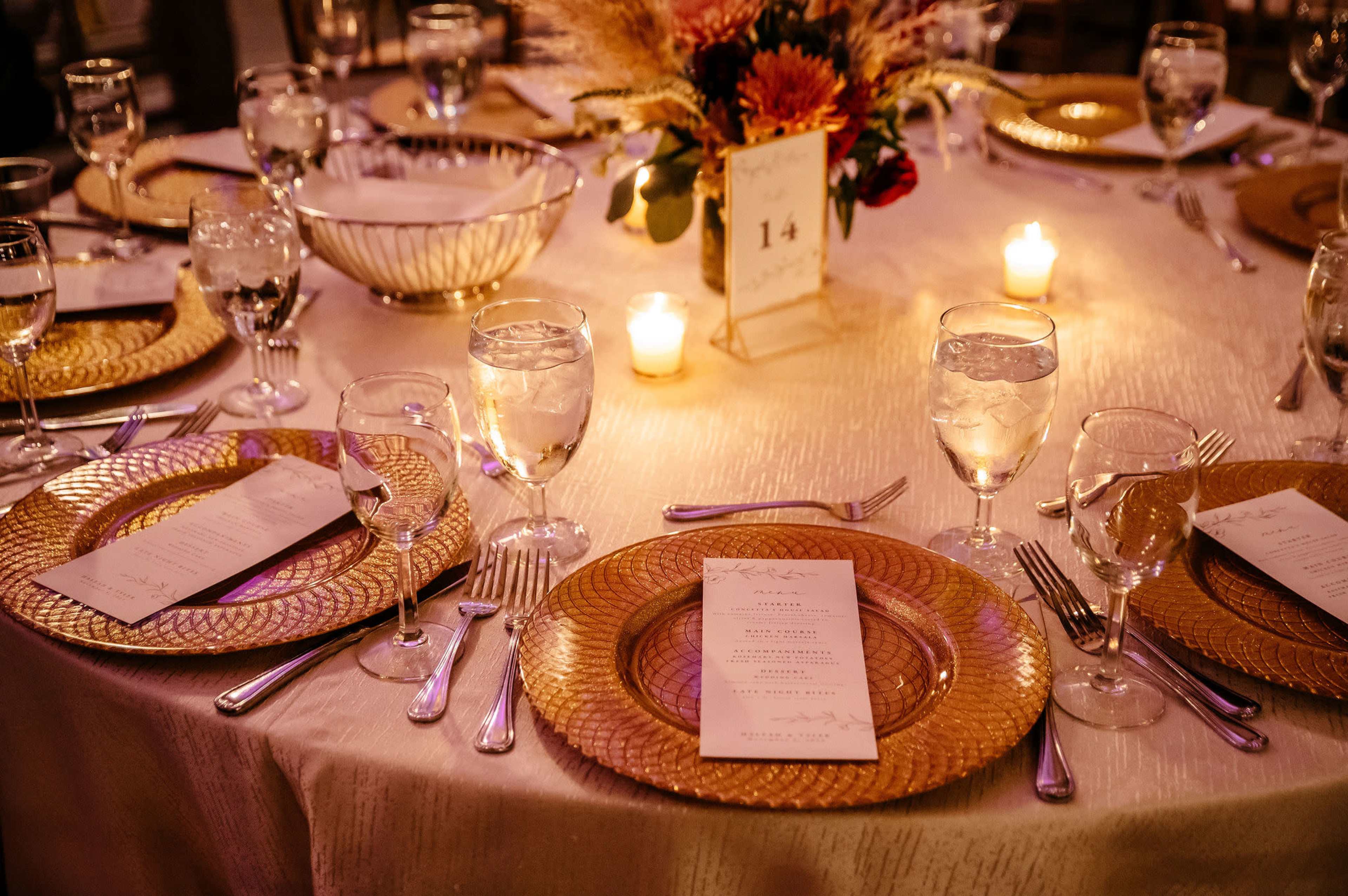 The image shows a dining table set with elegant place settings, menu cards, water glasses, and a floral centerpiece surrounded by lit candles.