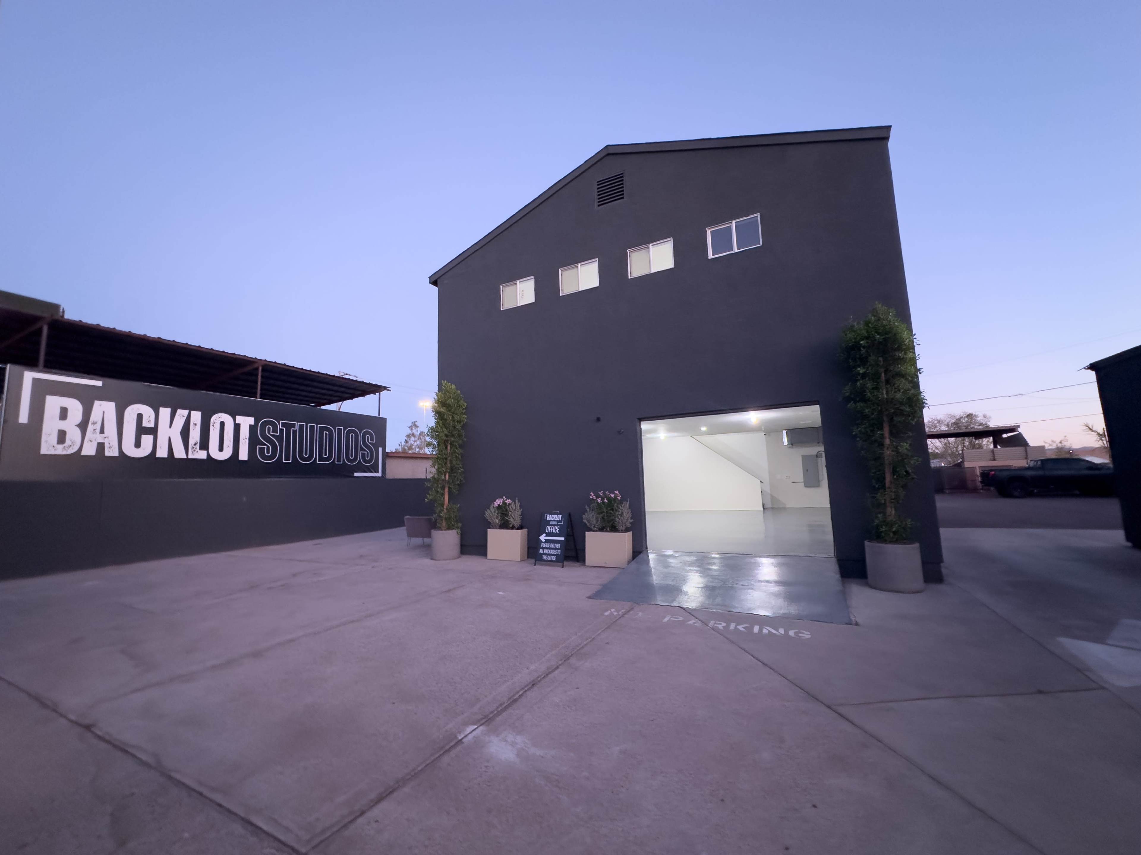 The exterior of Backlot Studios, featuring a dark building with a large open garage door and landscaped planters at the entrance.
