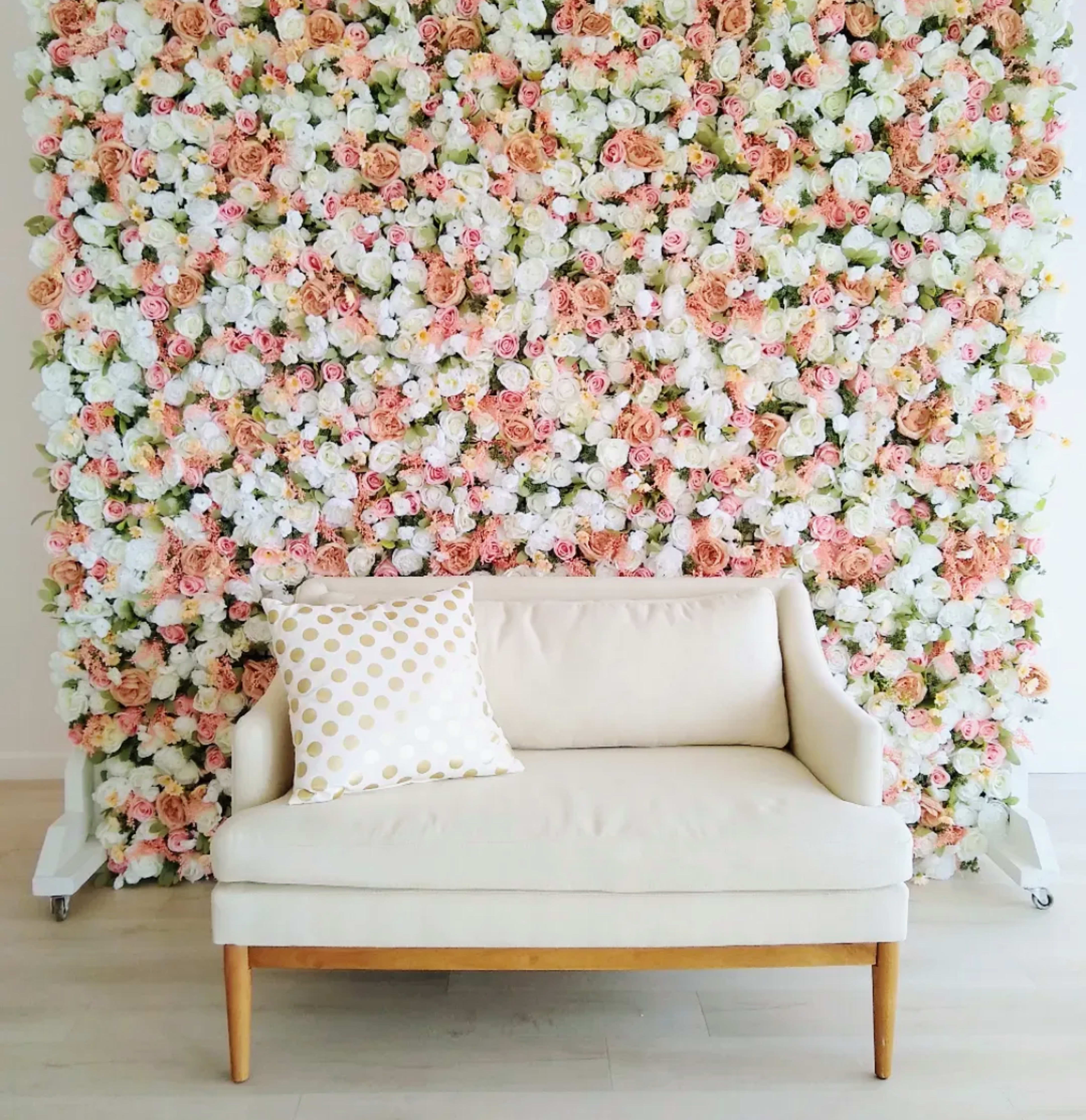 A beige sofa with wooden legs is positioned in front of a backdrop of pink and white floral decorations.
