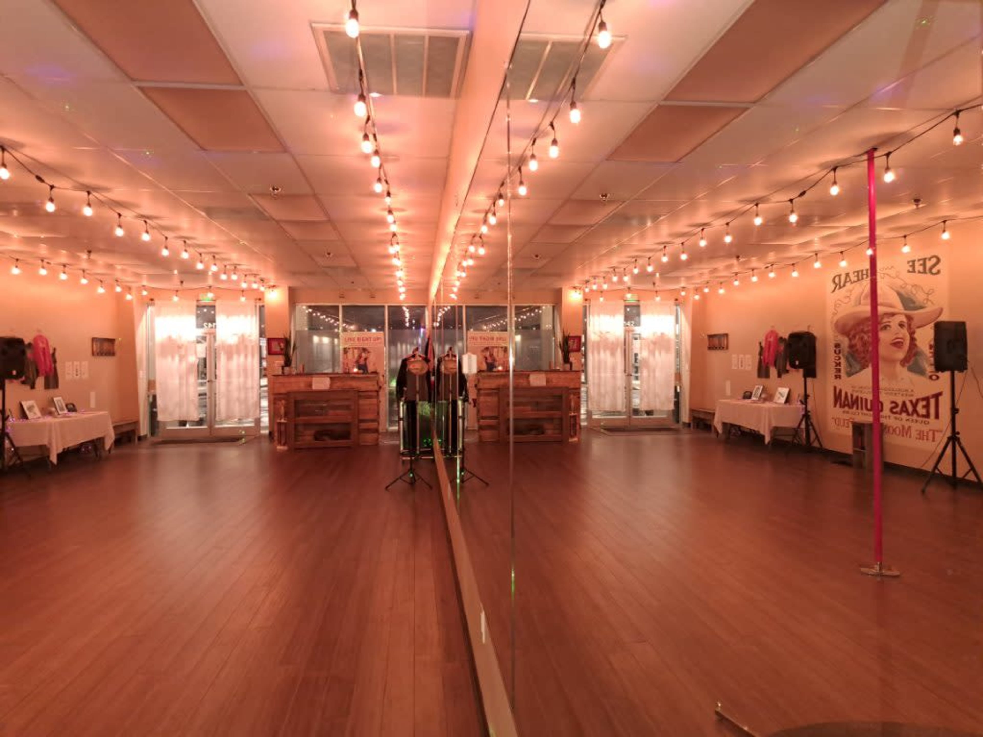 A dance studio featuring a large mirror, wooden flooring, and string lights illuminating the space.