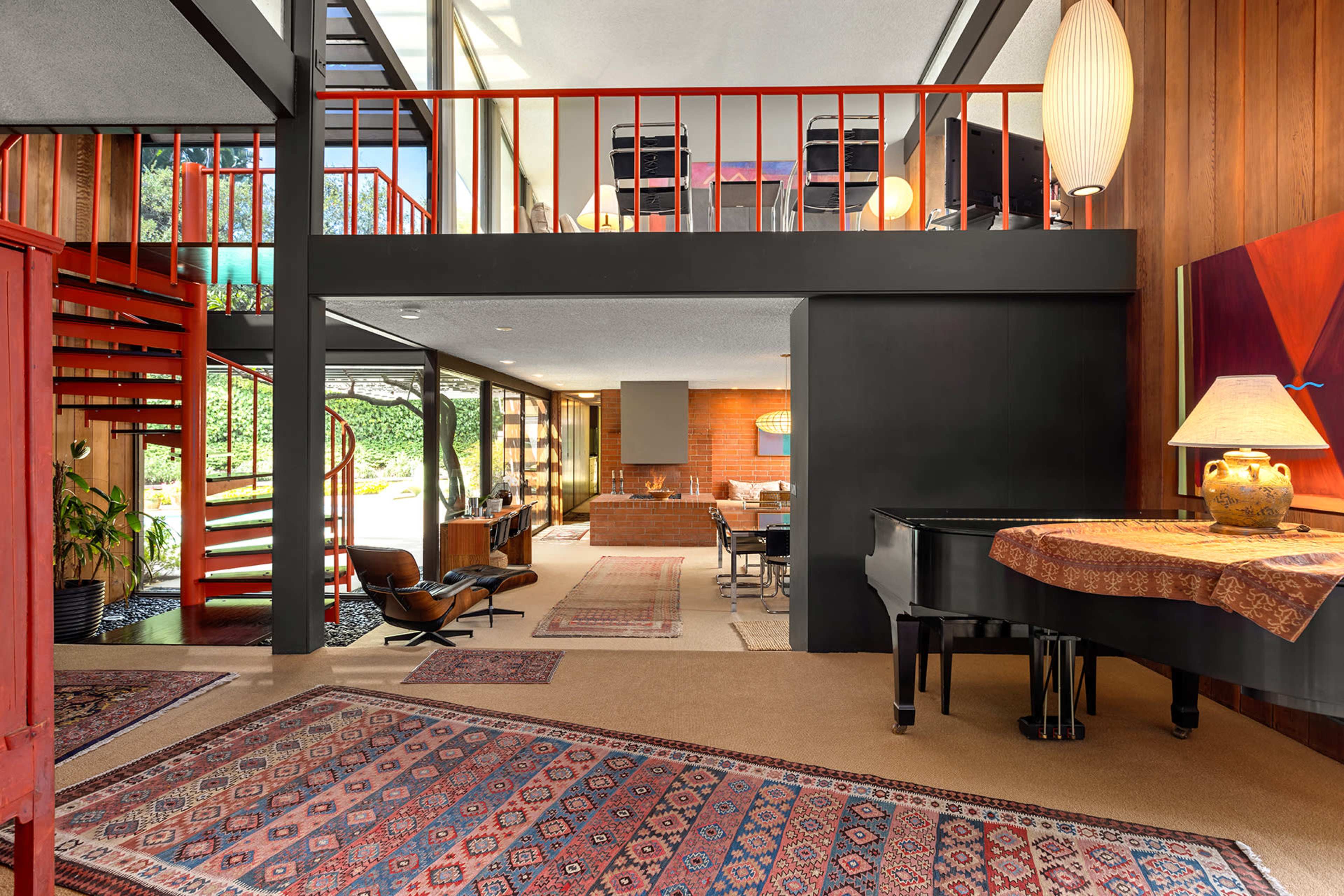 The interior features a modern open-concept space with a staircase, a grand piano, and a view of the dining area through large windows.