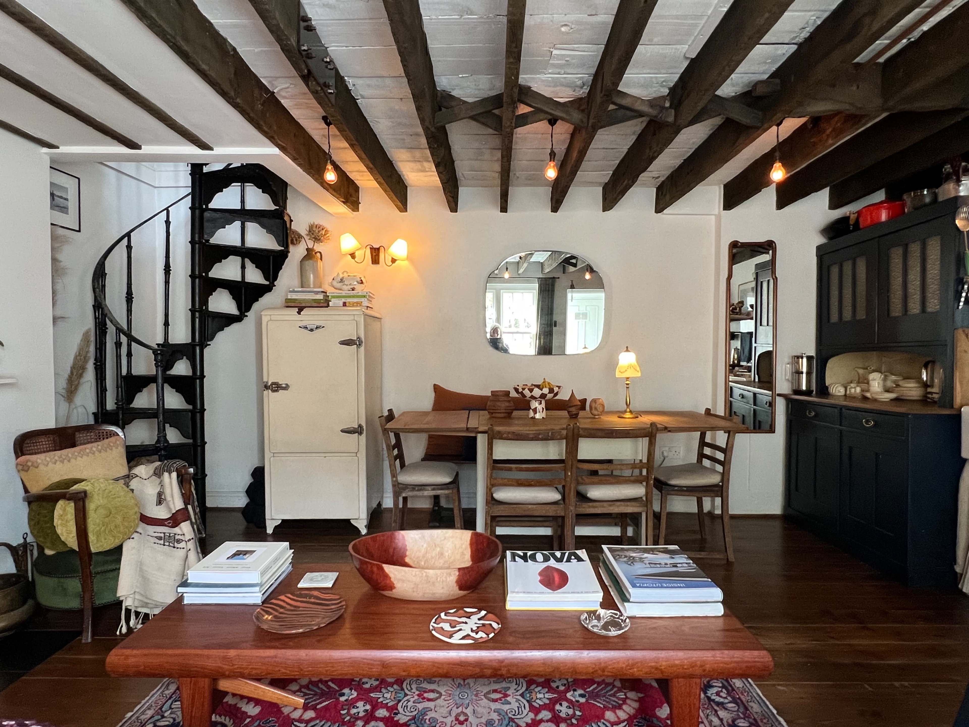 A cozy living space featuring a wooden dining table surrounded by chairs, a spiral staircase in the corner, and various decorative items on the table and shelves.