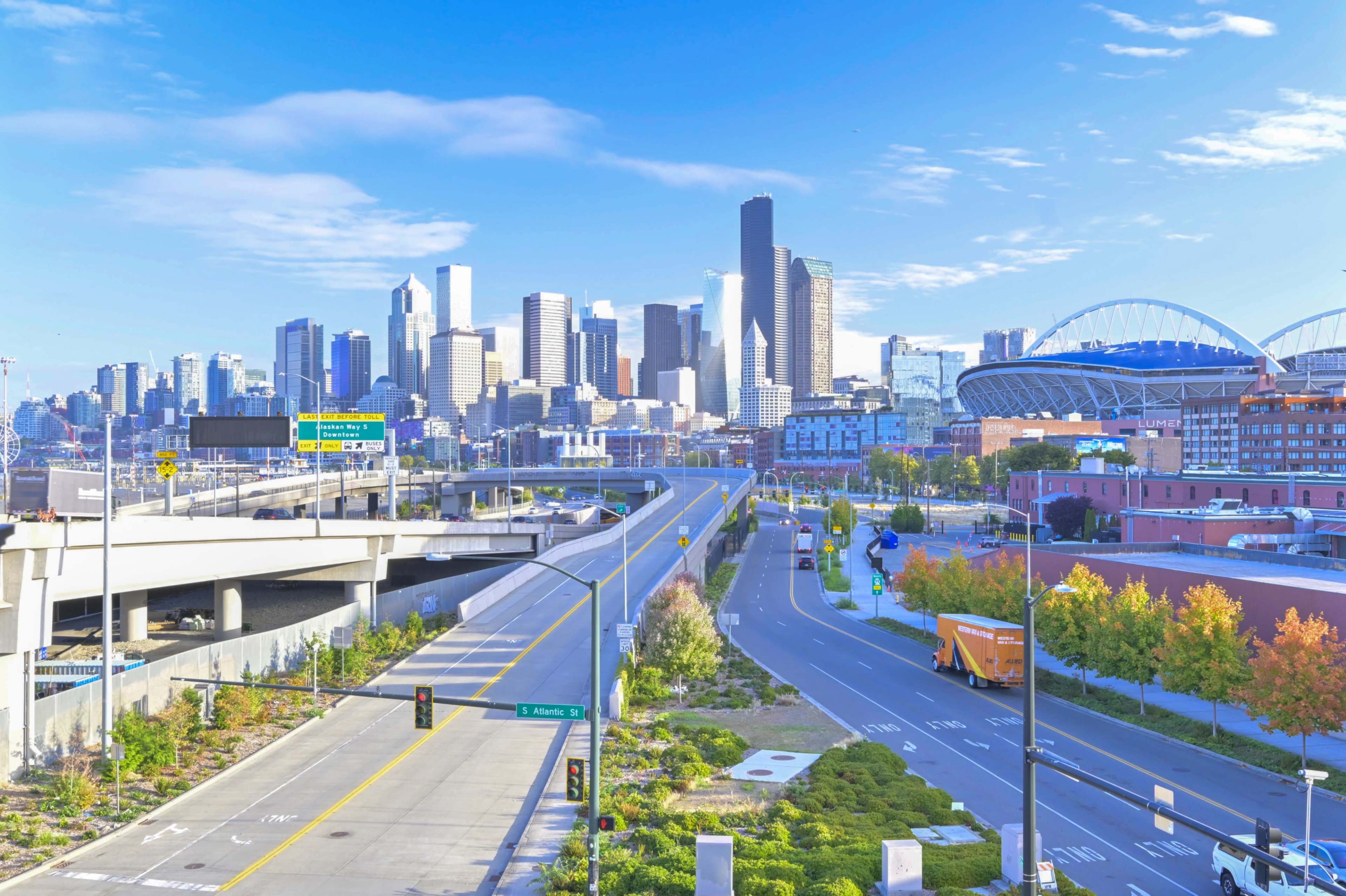 A clear view of a modern city skyline featuring tall buildings, with empty roadways and greenery in the foreground.