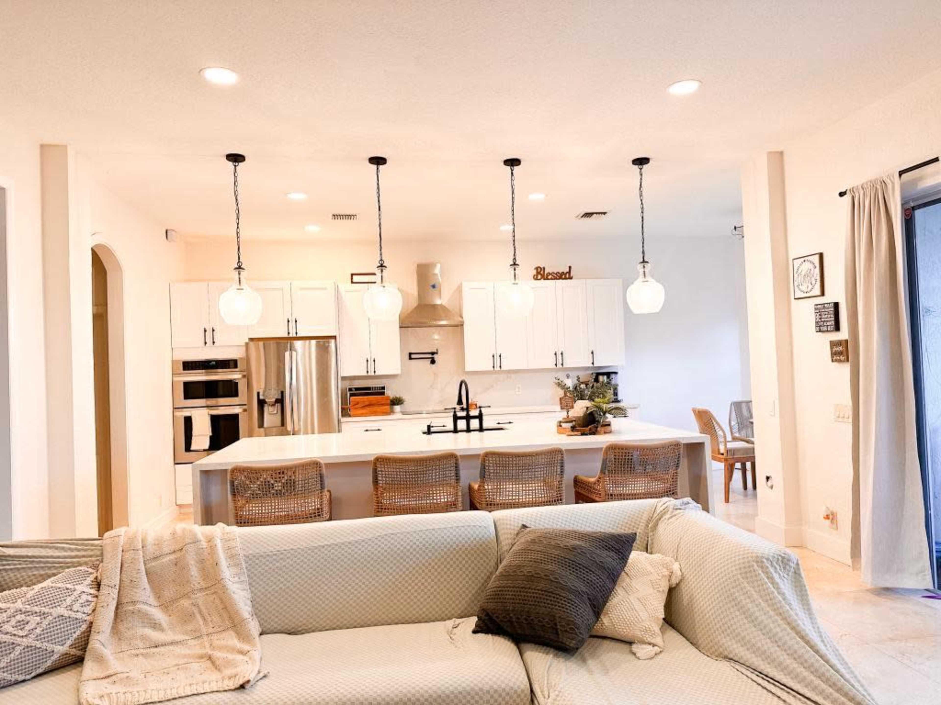 A modern kitchen with white cabinets, a large island featuring bar stools, and pendant lighting hangs above the space.