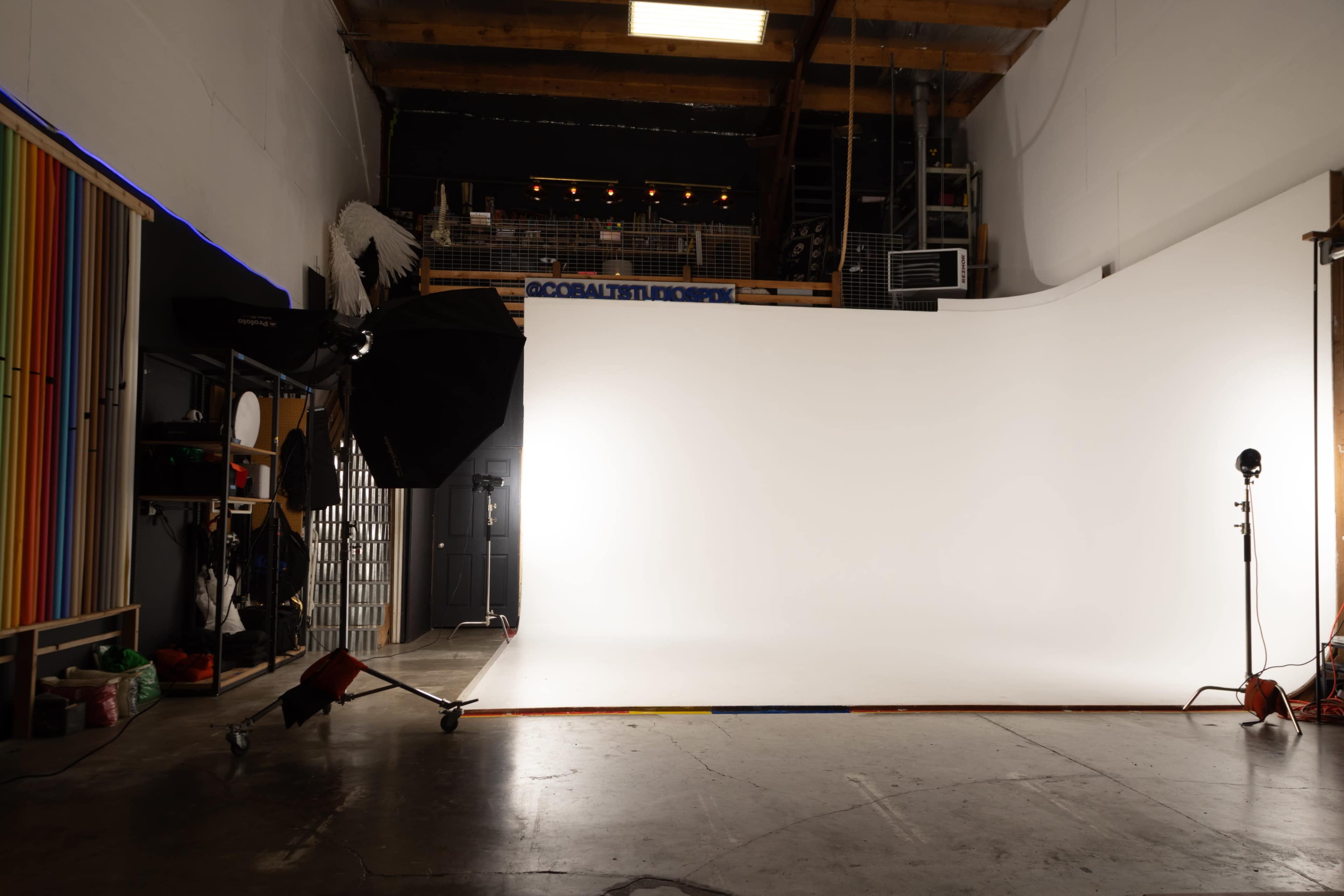 A photography studio is set up with a white backdrop, large lighting equipment, and various props organized on shelves.