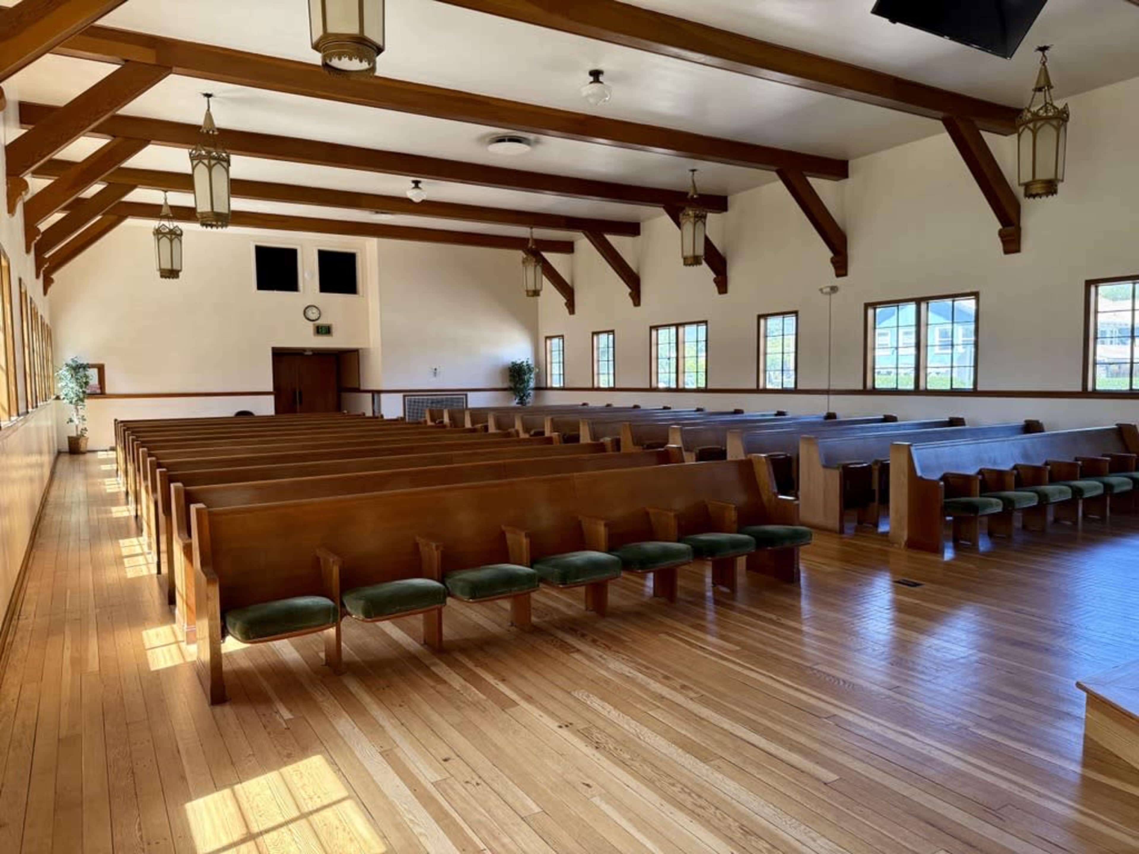 The image shows a spacious church interior with wooden pews arranged in rows beneath exposed beam ceilings and large windows.