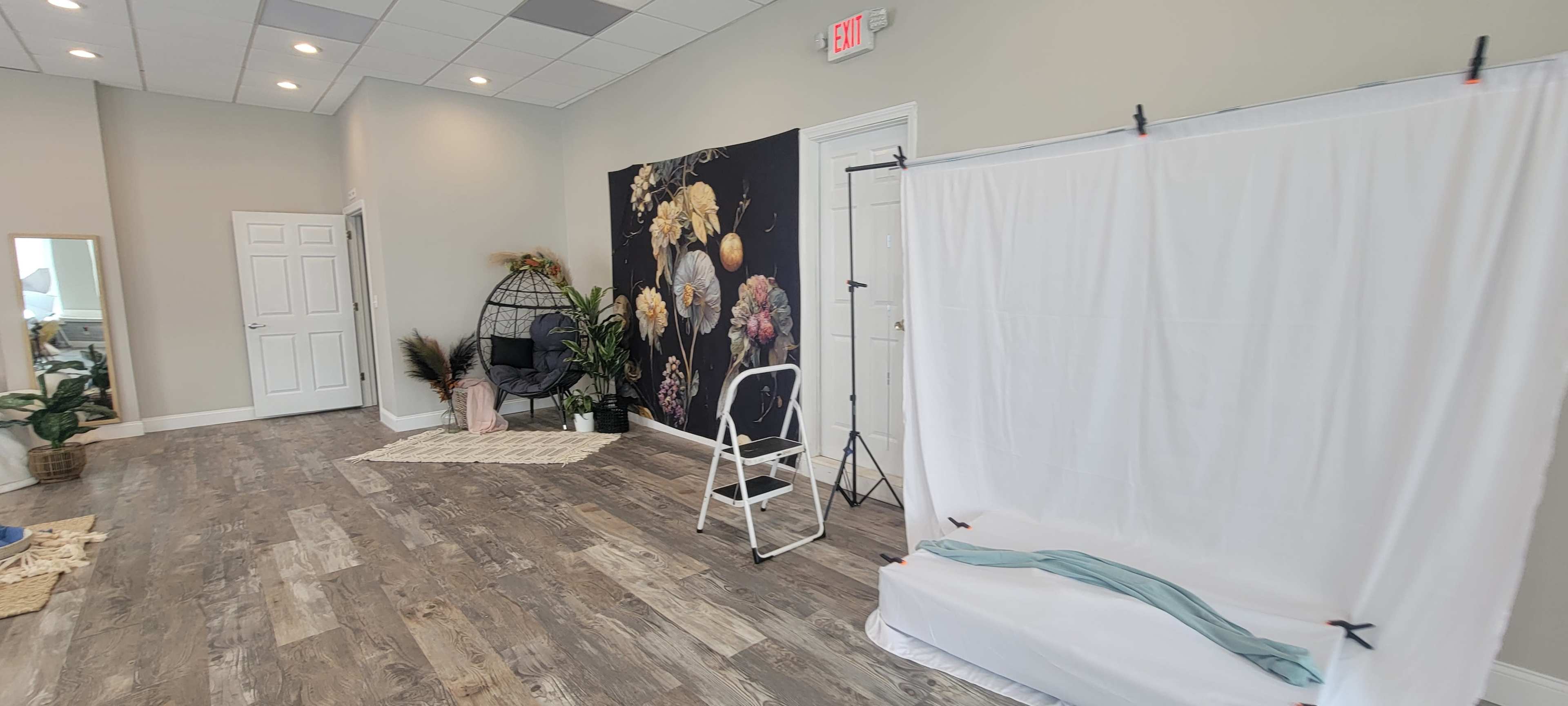 A spacious room with a floral mural on the wall, a white backdrop setup, a hanging chair, and light wooden flooring.