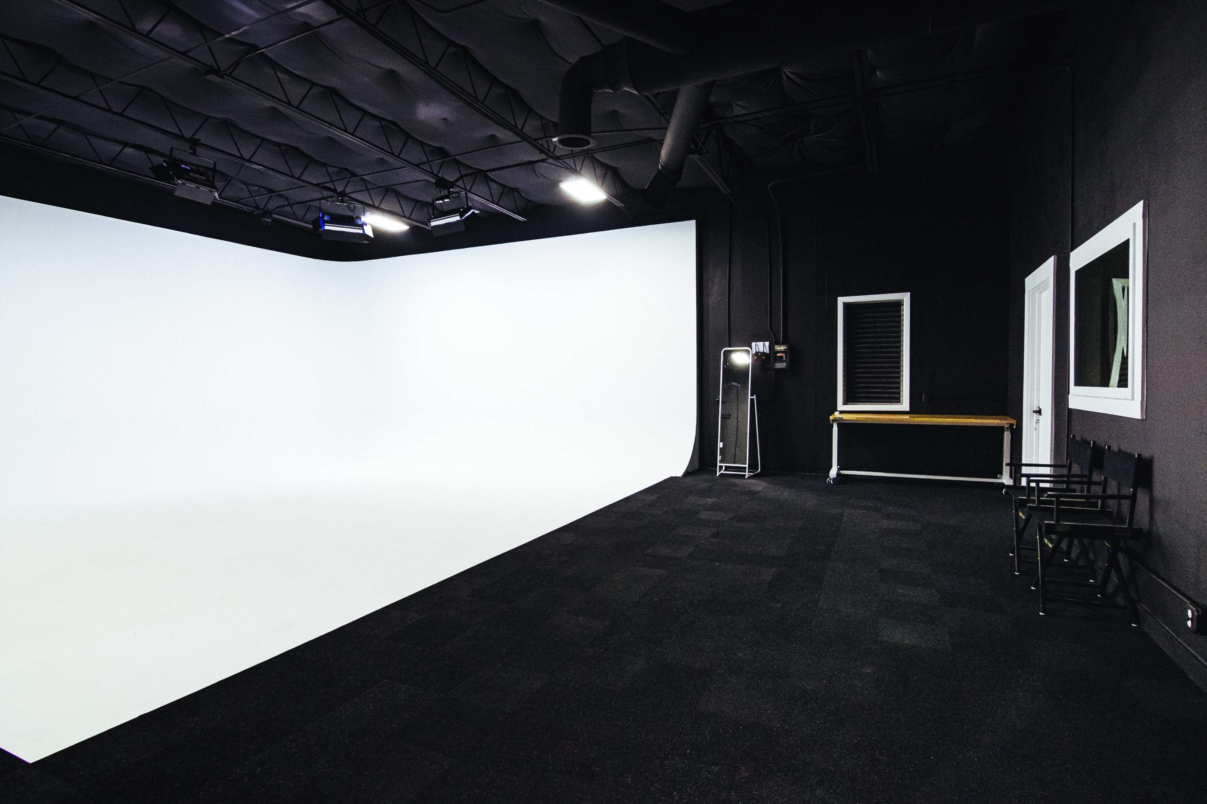 A spacious studio with a white backdrop, black flooring, and minimalist furnishings, including a table and chairs.