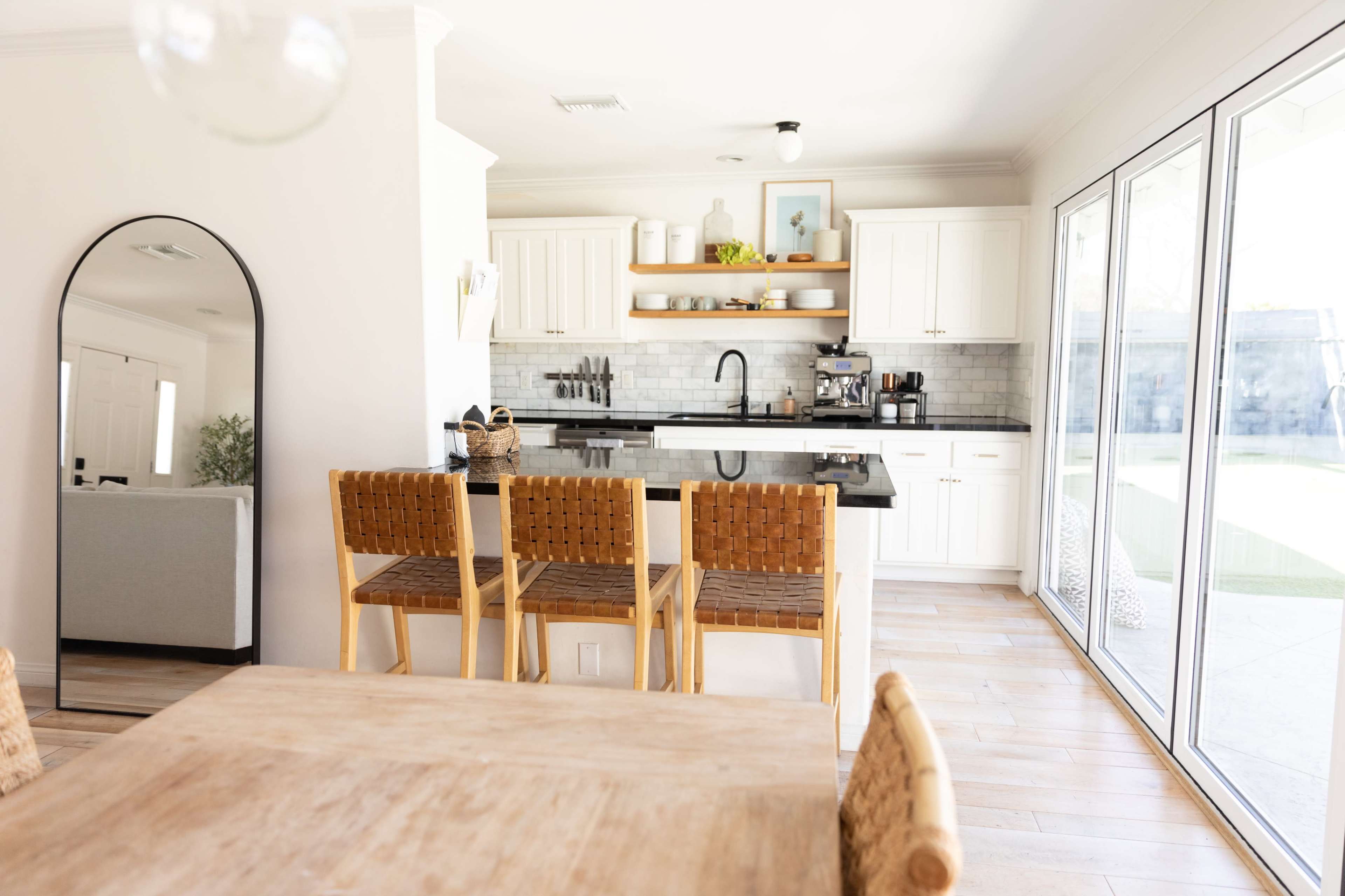 The image shows a modern kitchen and dining area with a large island, barstools, and sliding glass doors leading to an outdoor space.