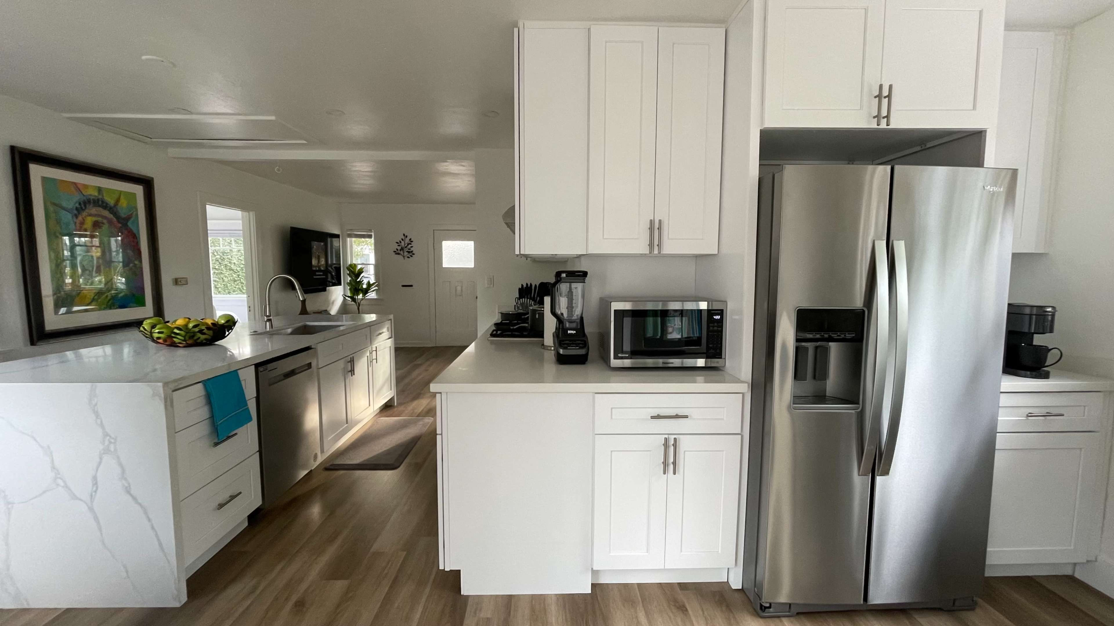 A modern kitchen with white cabinetry, stainless steel appliances, and a large island with a marble countertop.