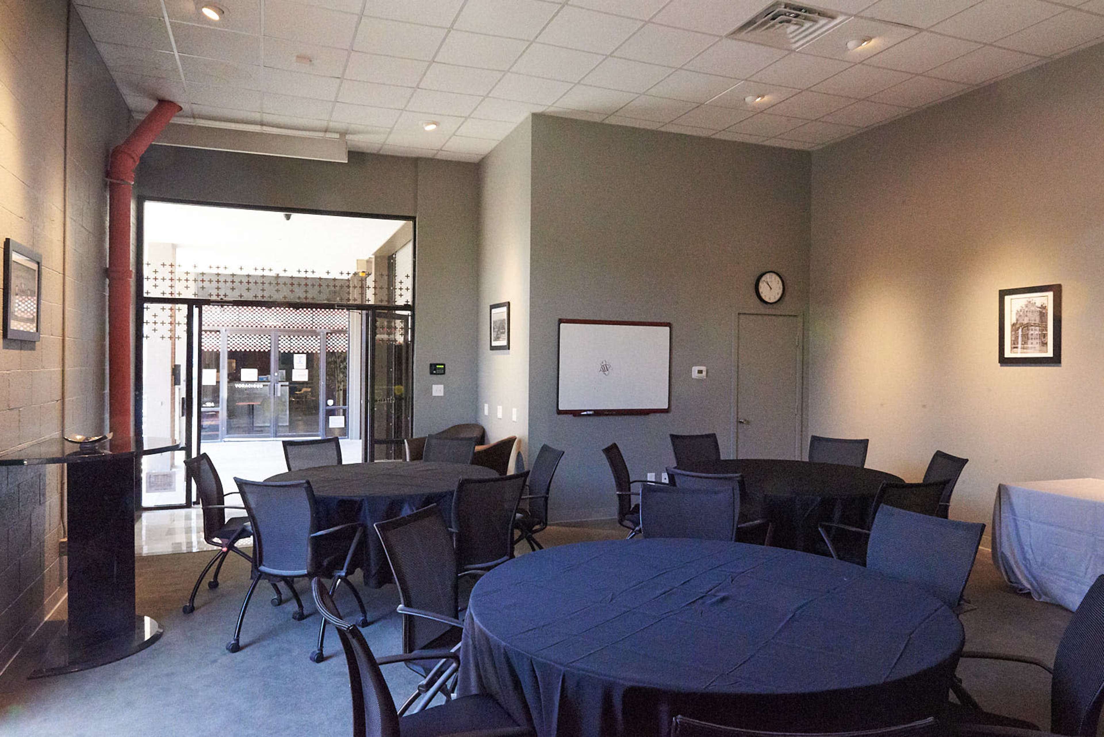 A meeting room with round tables covered in dark tablecloths and large windows revealing an outdoor area.