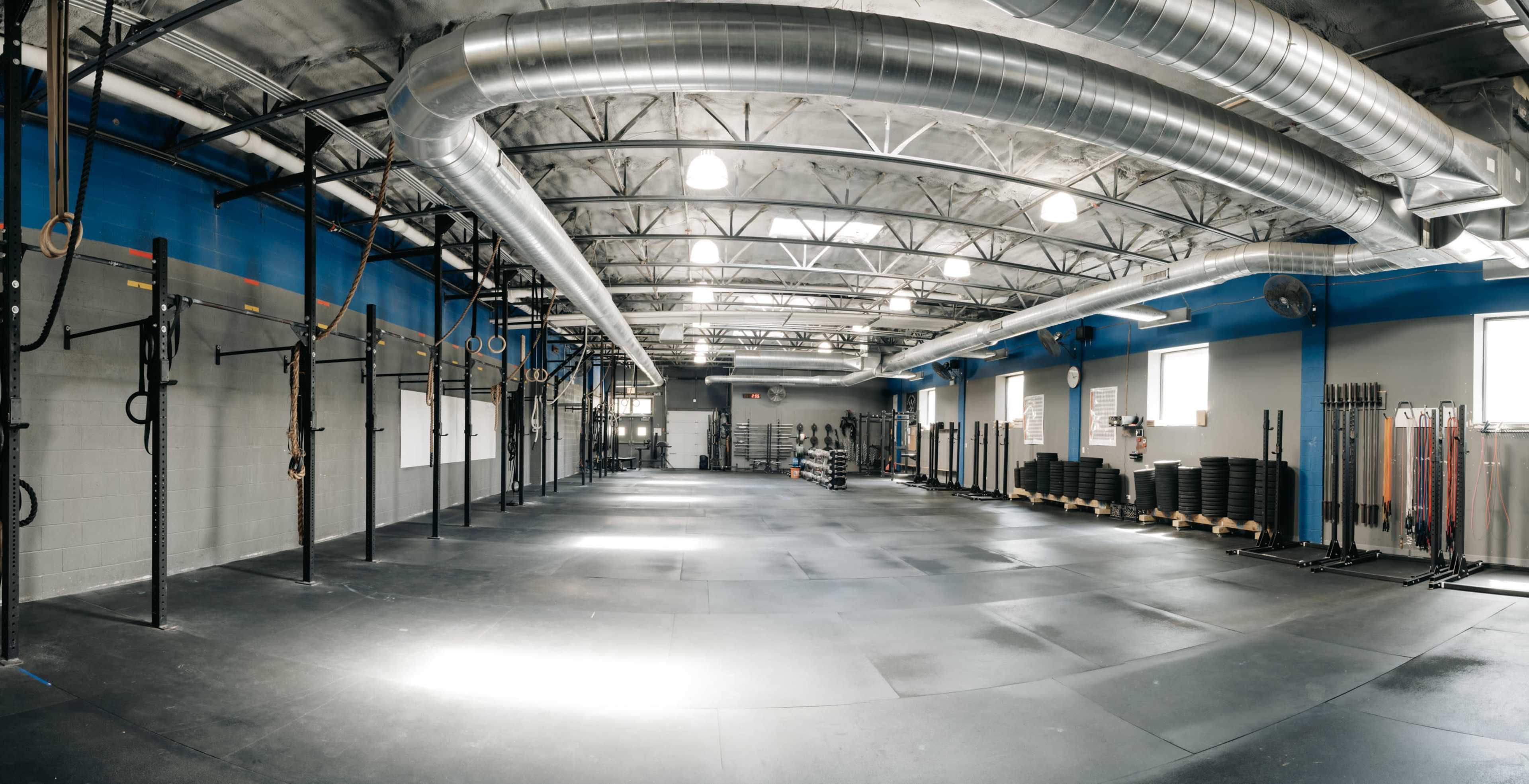 A spacious gym features black rubber flooring, wall-mounted pull-up bars, and neatly stacked weight plates along one side.